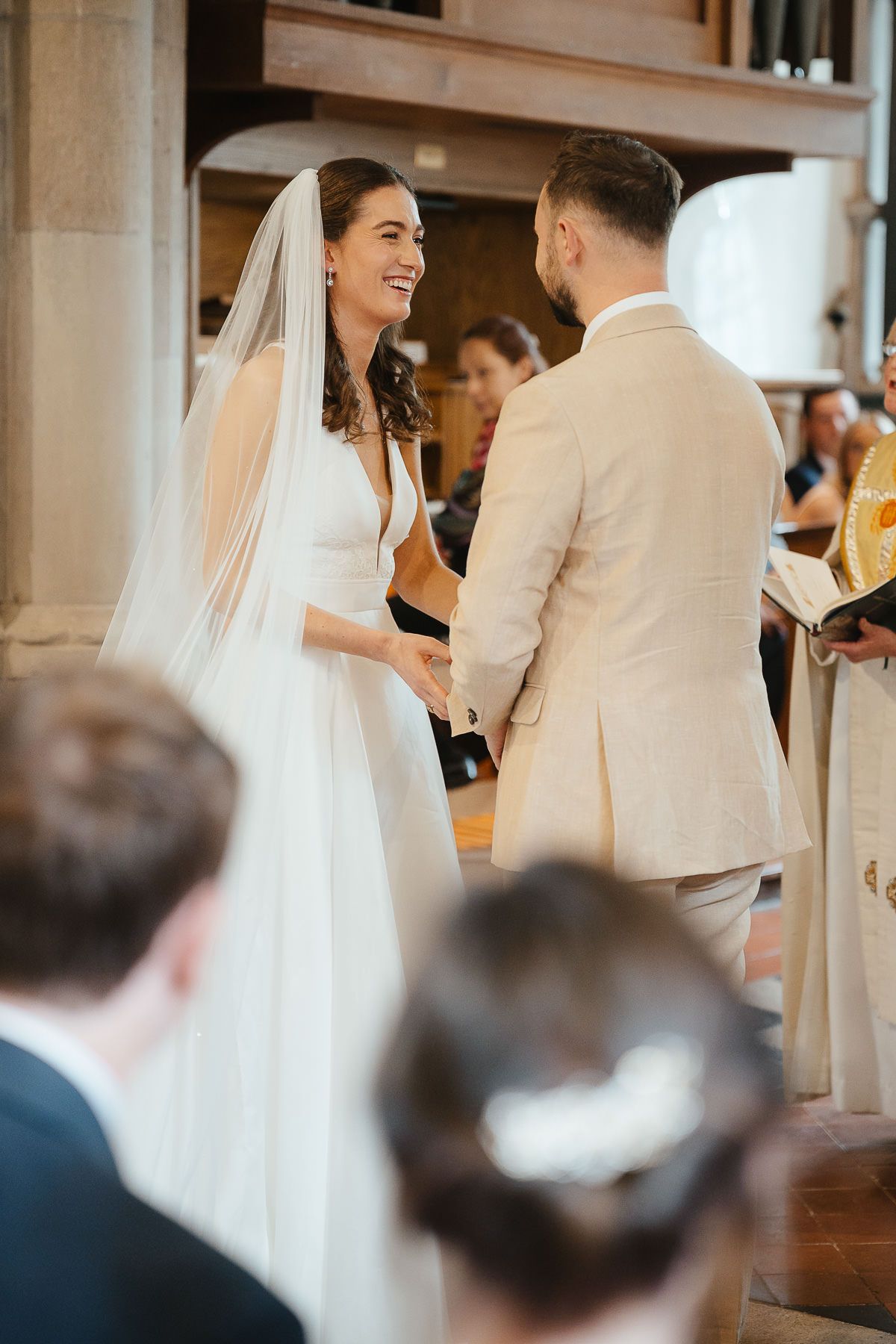 A joyful wedding ceremony moment captured in a light-filled chapel as a couple holds hands at the altar.