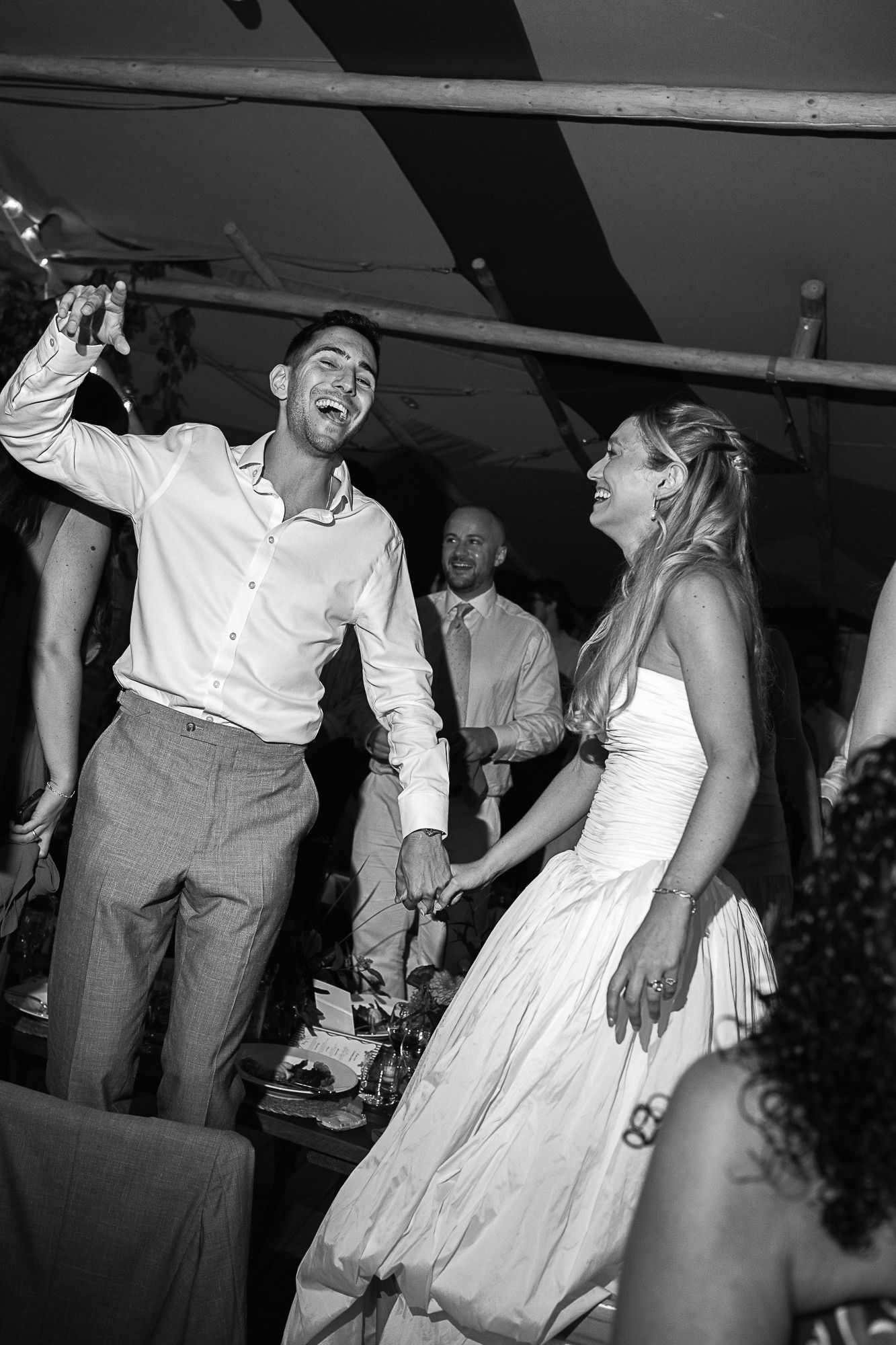 Black and white photo of joyful bride and groom dancing together at their wedding reception celebration.
