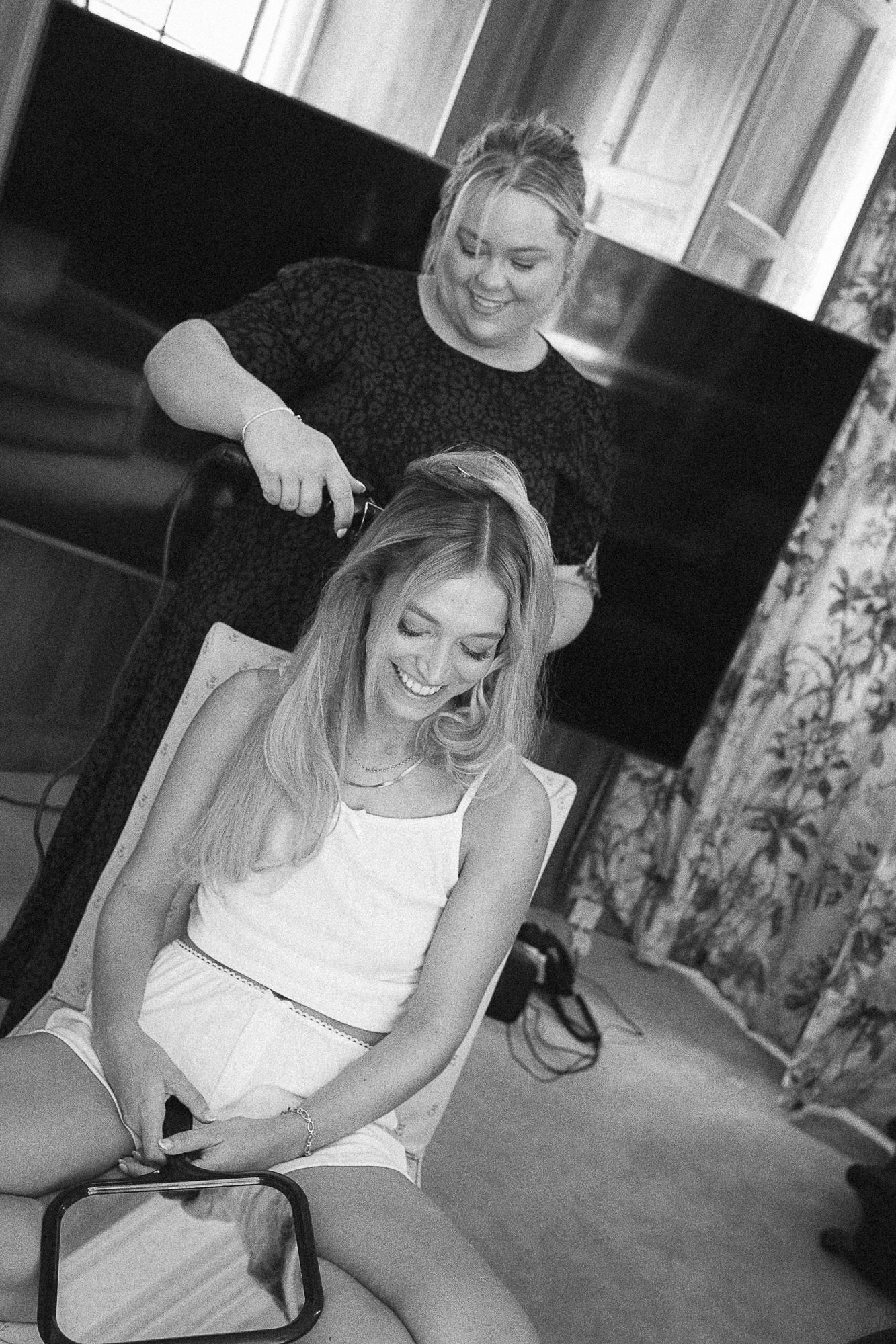 Hairstylist styling blonde bride's hair before wedding in black and white photo.