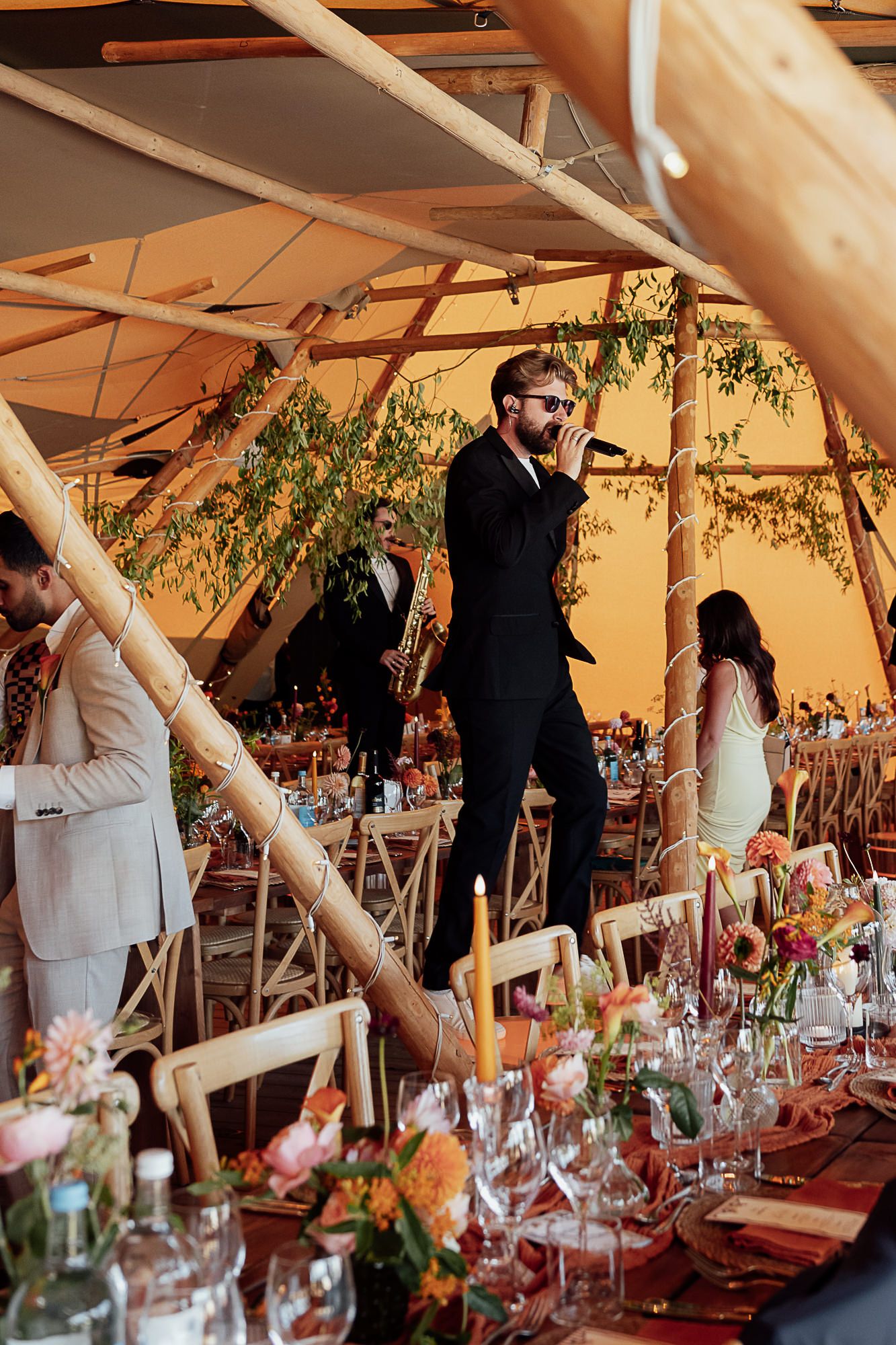 Singer performing at an elegant outdoor wedding reception under a tipi tent with floral centerpieces.
