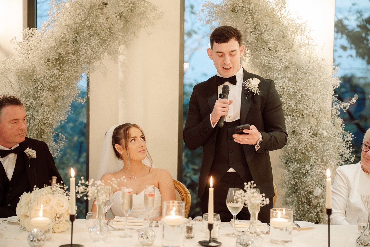 A wedding reception table features elegant white floral arrangements and candlelight creating a romantic atmosphere.