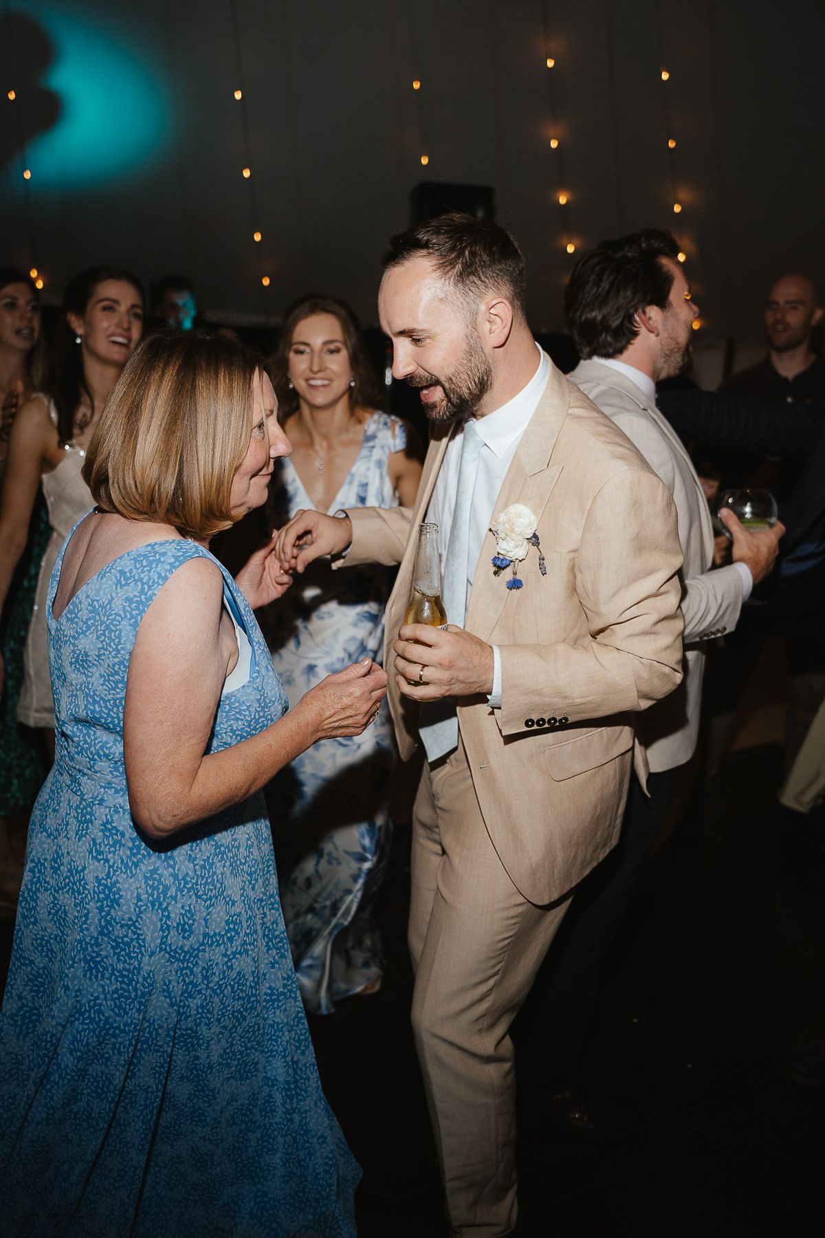 A couple dancing together at a party, with one person wearing a blue dress and another in a beige suit.