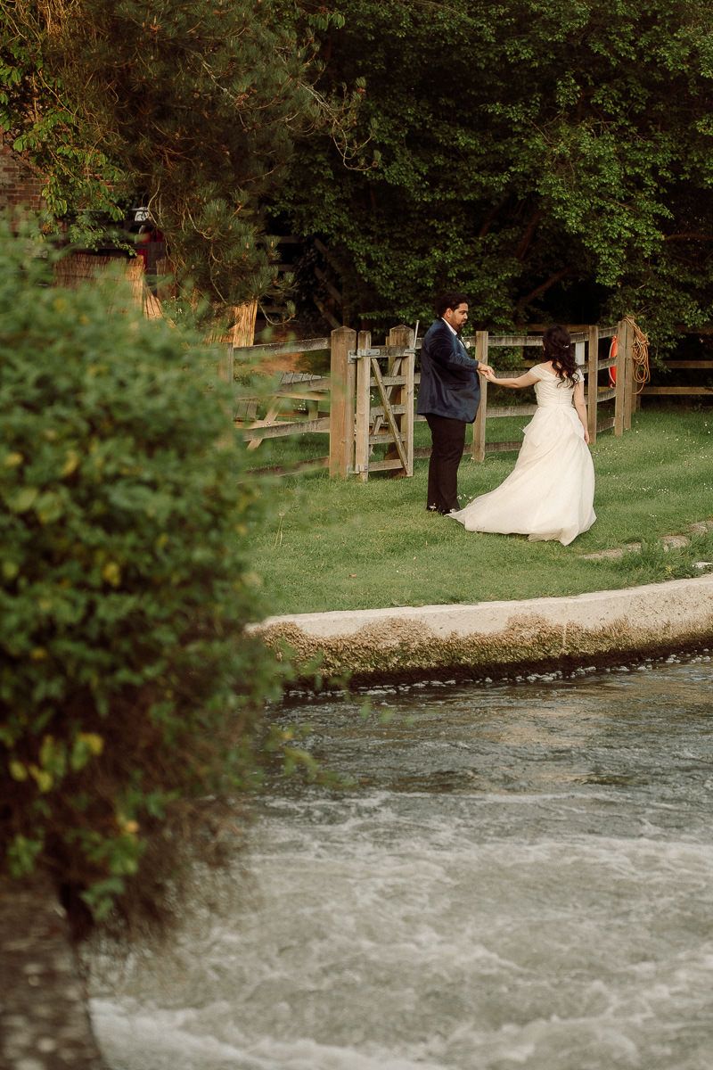 A couple in wedding attire poses near a rushing river in a scenic outdoor setting.