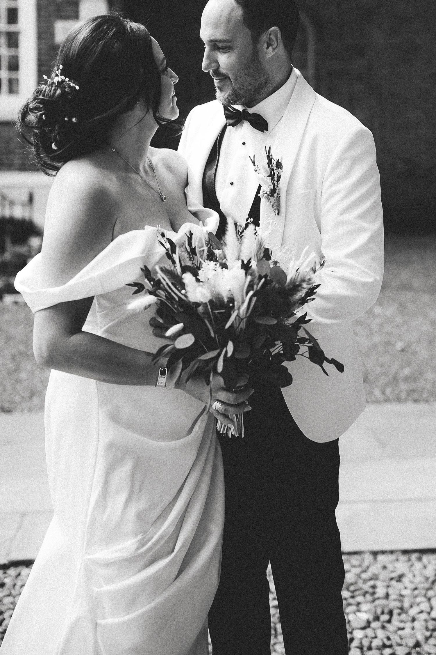A tender black and white wedding moment showing a couple in formal attire with the bride holding a floral bouquet.