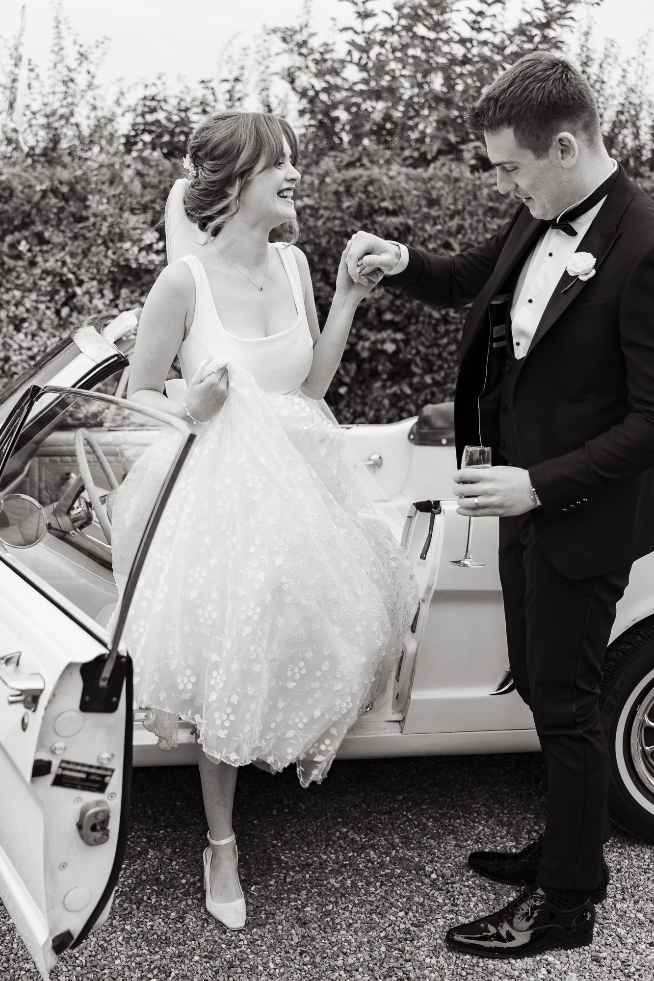 A vintage-inspired wedding moment captured in black and white with a tea-length dress and classic car in the background  at Larkspur Lodge