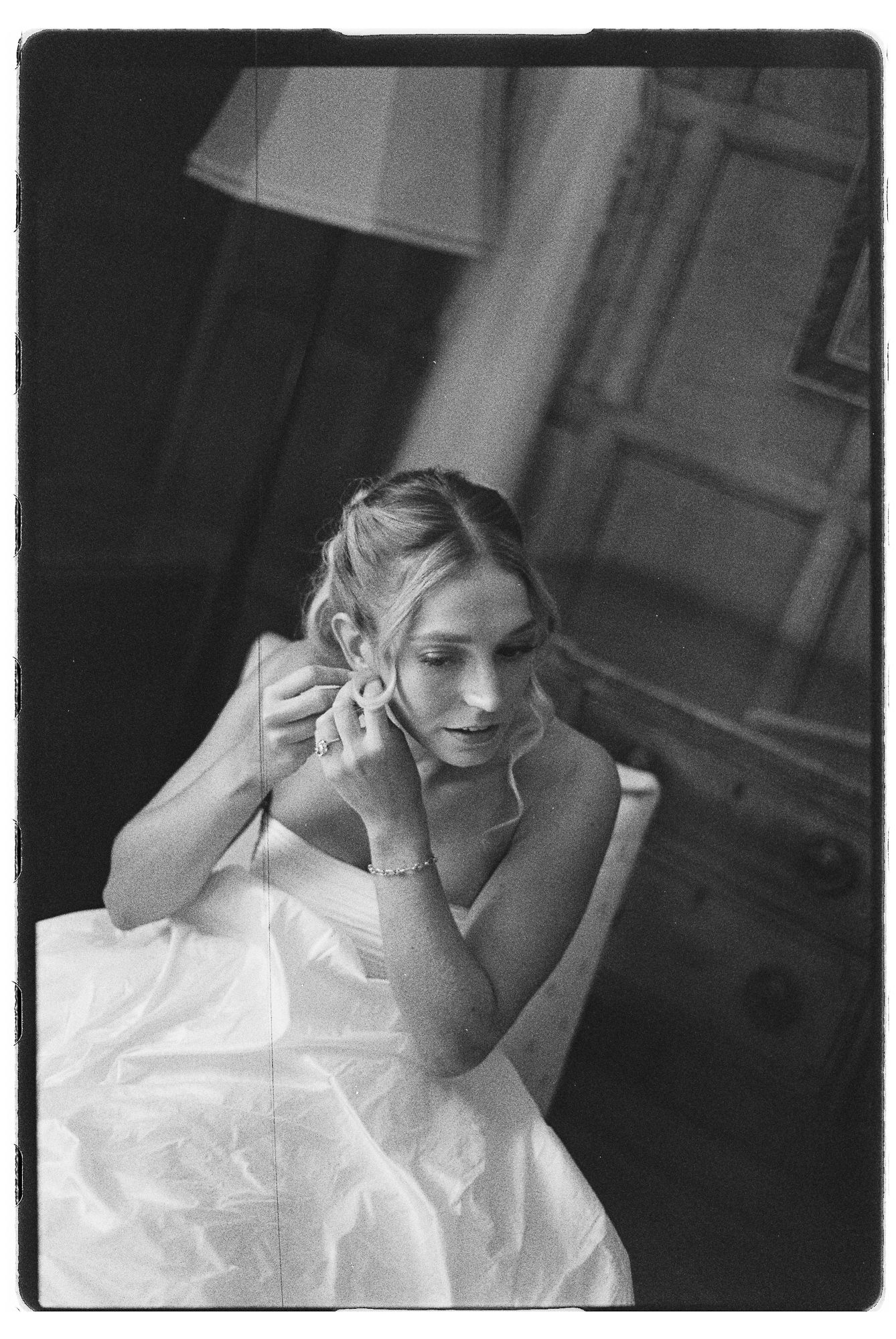 Black and white photo of bride in white gown putting on earring while getting ready for her wedding day.