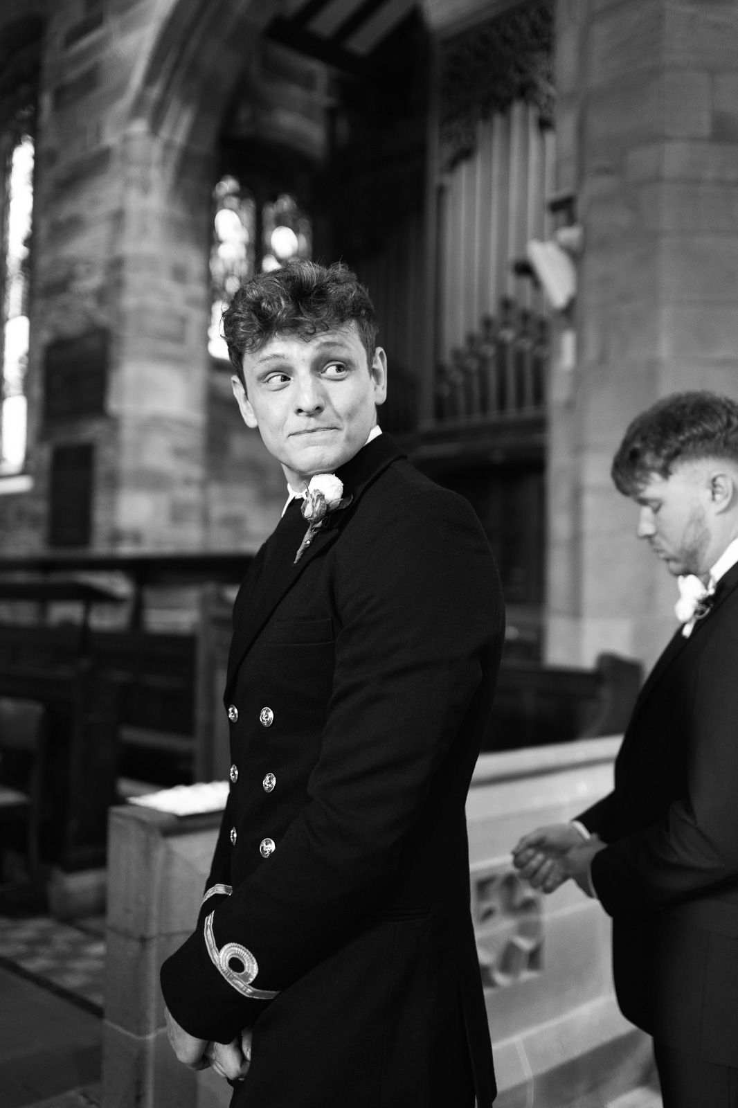 Black and white photo of a groom in military uniform glancing back inside a historic stone church.