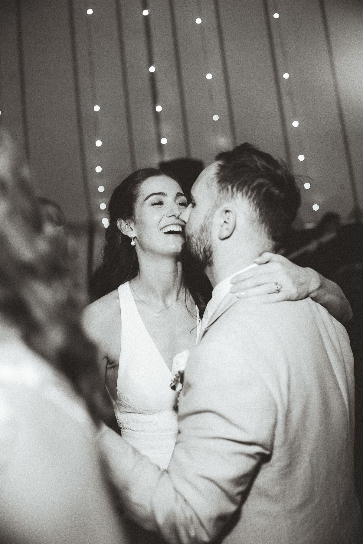A joyful couple shares a dance moment at their wedding reception with string lights twinkling in the background.
