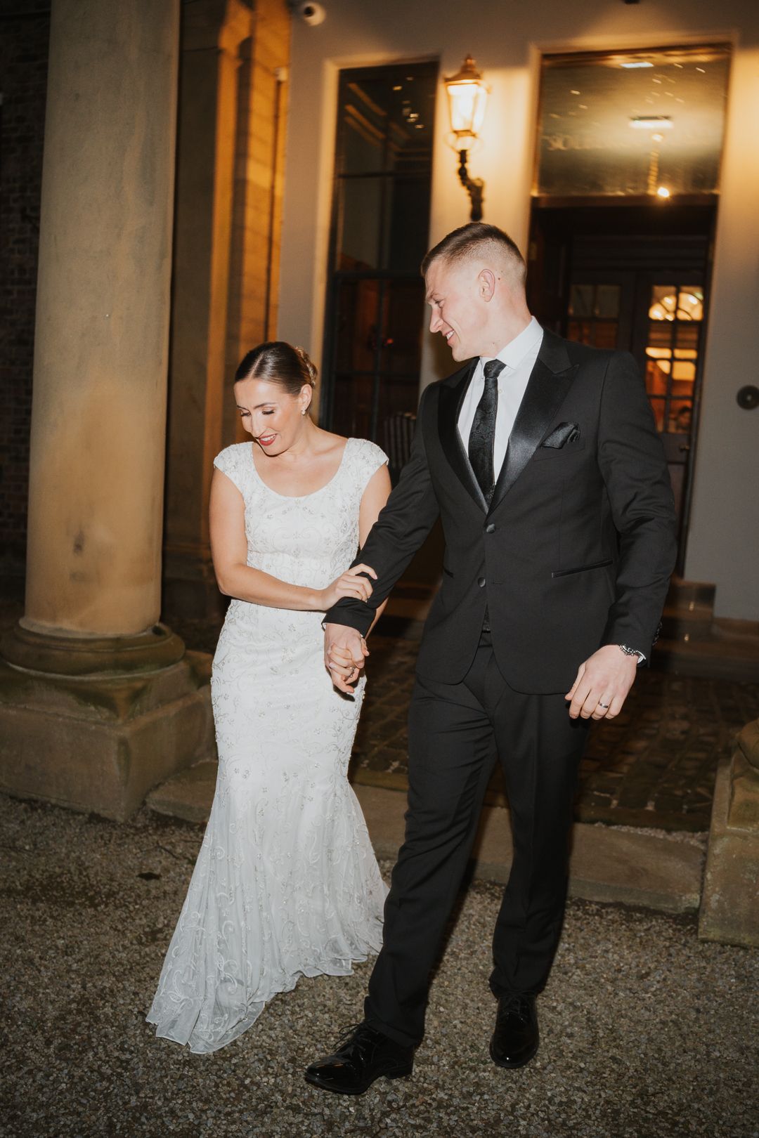Couple in wedding attire dances together outdoors at night with soft lighting and gravel underfoot.