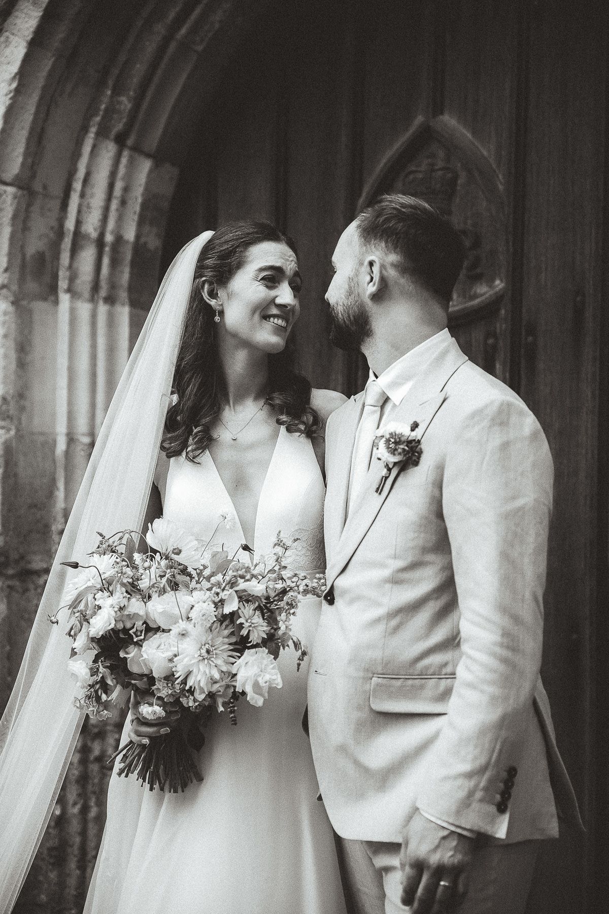 Black and white photo series captures romantic wedding couple moments outside a church with bouquet and veil.
