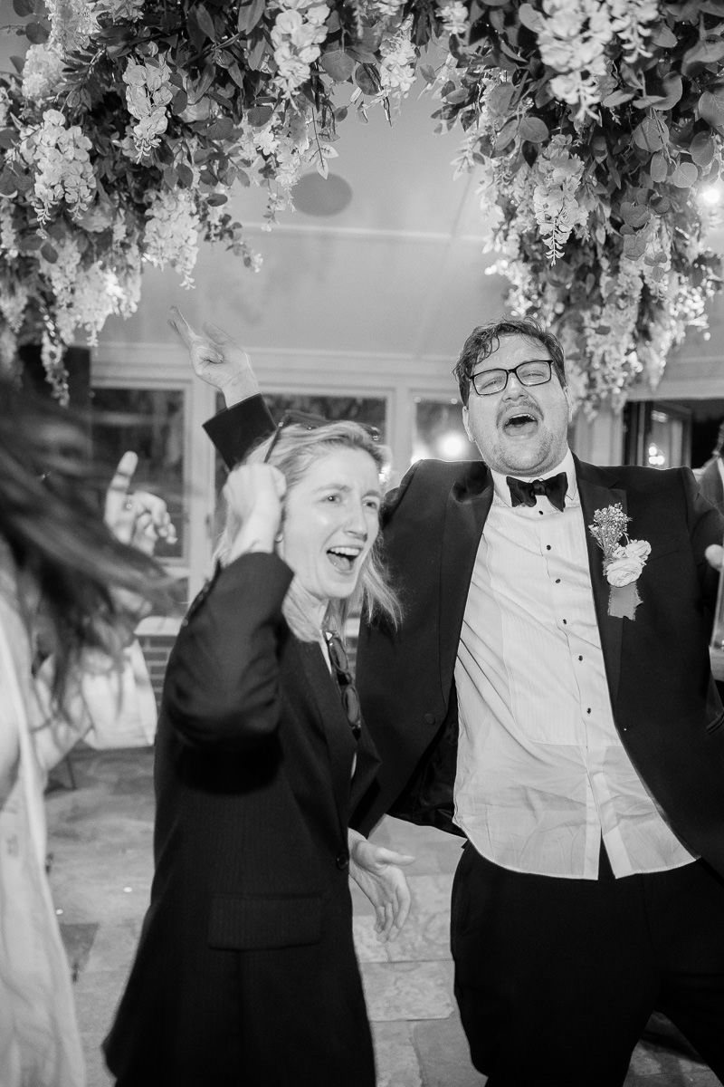 Black and white photos capturing celebratory moments with guests laughing and cheering at an elegant wedding reception.