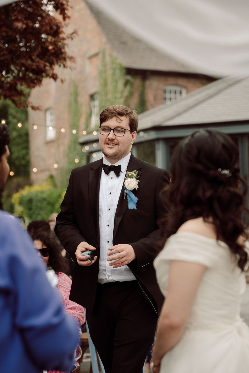 Wedding celebration outdoors with string lights and formal attire at an elegant venue with brick building in background.