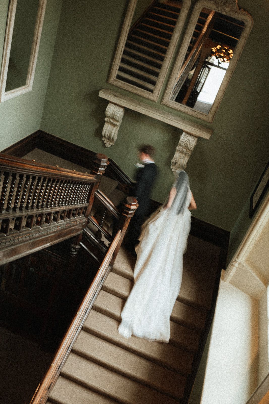 Bride and groom ascending grand staircase in elegant venue, bride's white gown trailing behind.