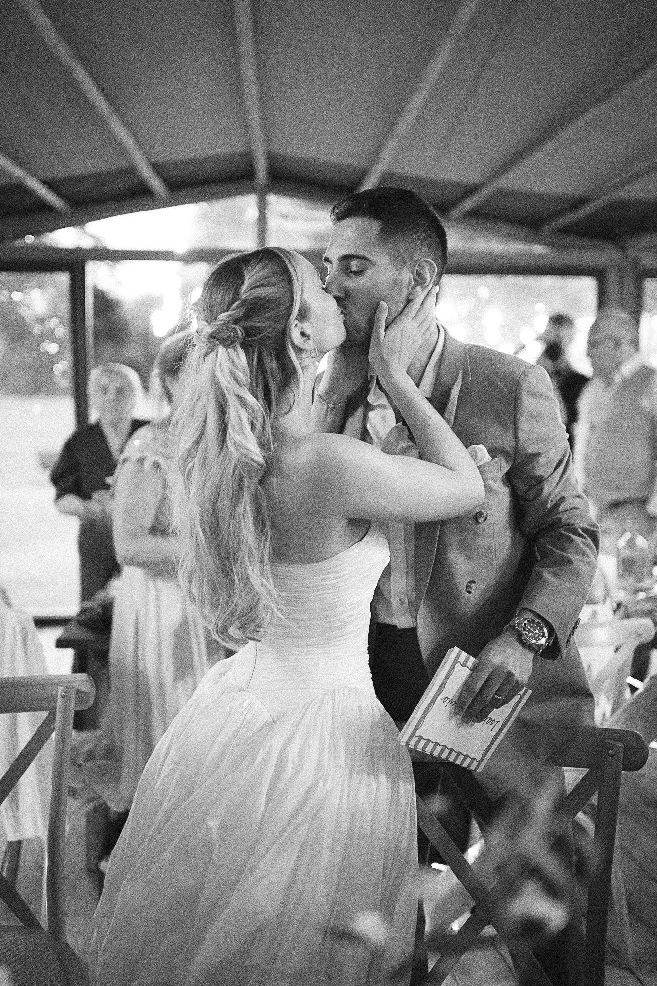 Black and white photo of a bride and groom sharing a romantic kiss at their wedding reception.