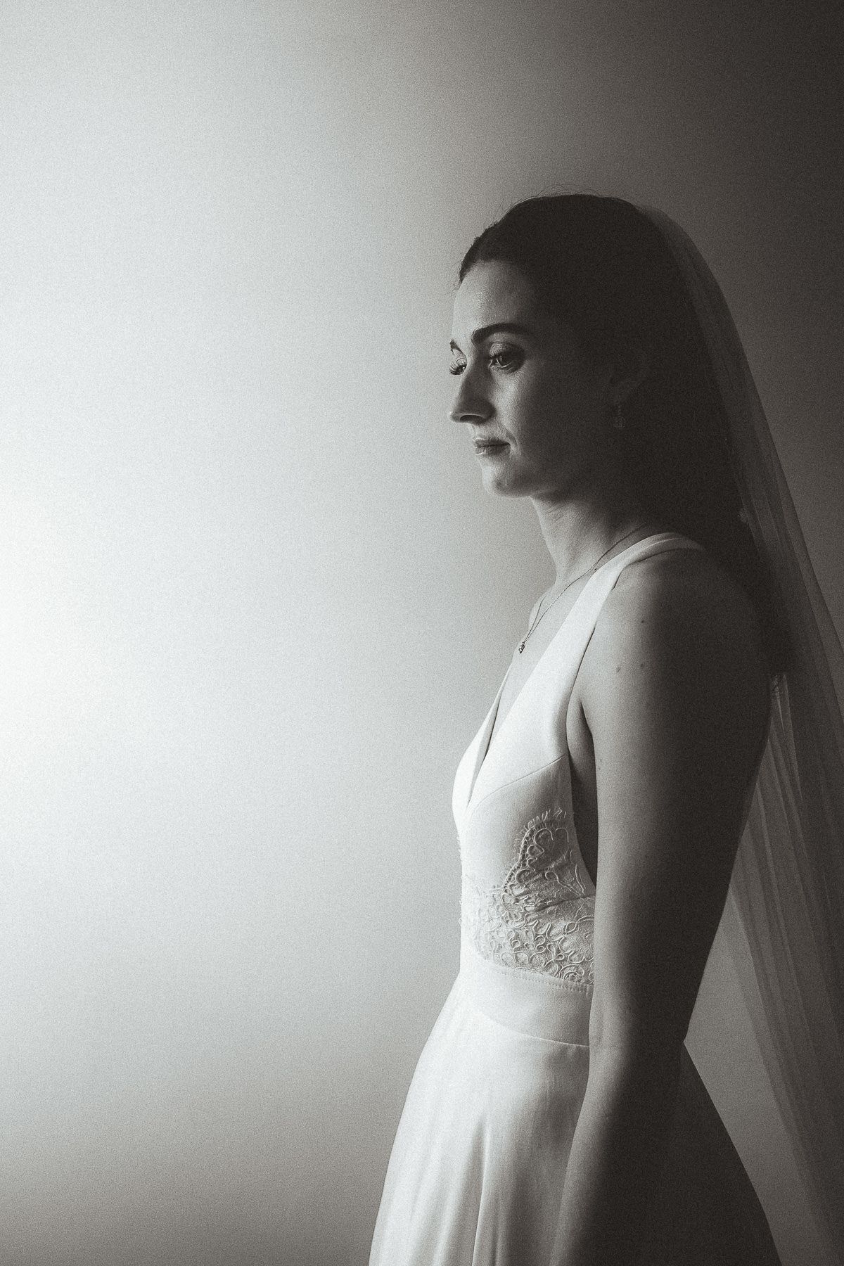 A dreamy black and white bridal portrait in profile view shows a bride wearing a delicate lace wedding gown with veil.
