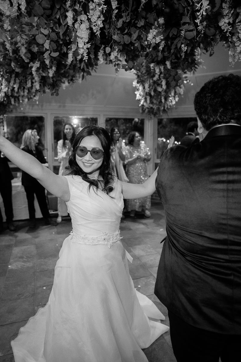 A young flower girl in a white dress dances joyfully at an outdoor wedding reception.