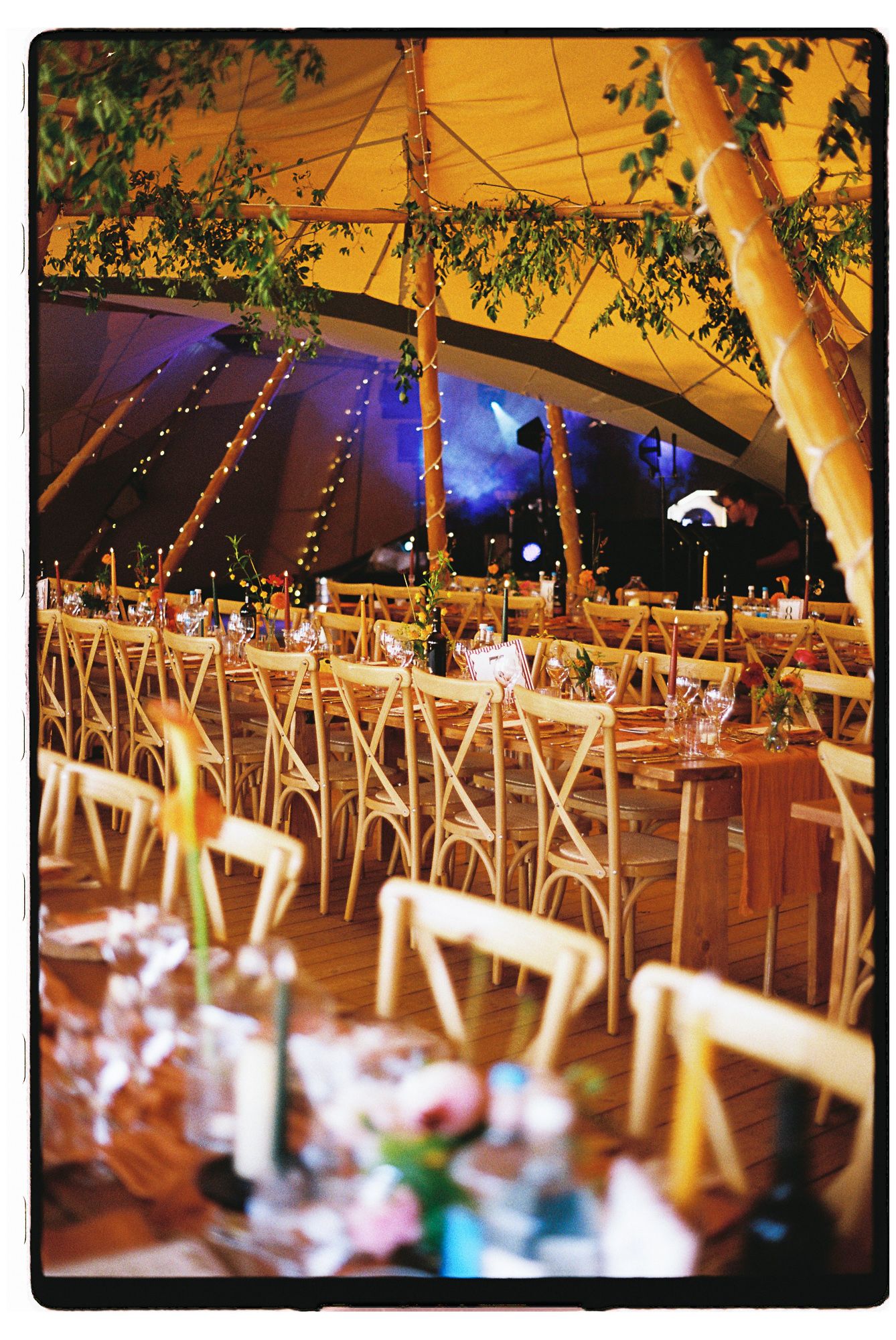 Elegant wedding reception inside a decorated tent with fairy lights, wooden chairs, and floral centerpieces on long dining tables.