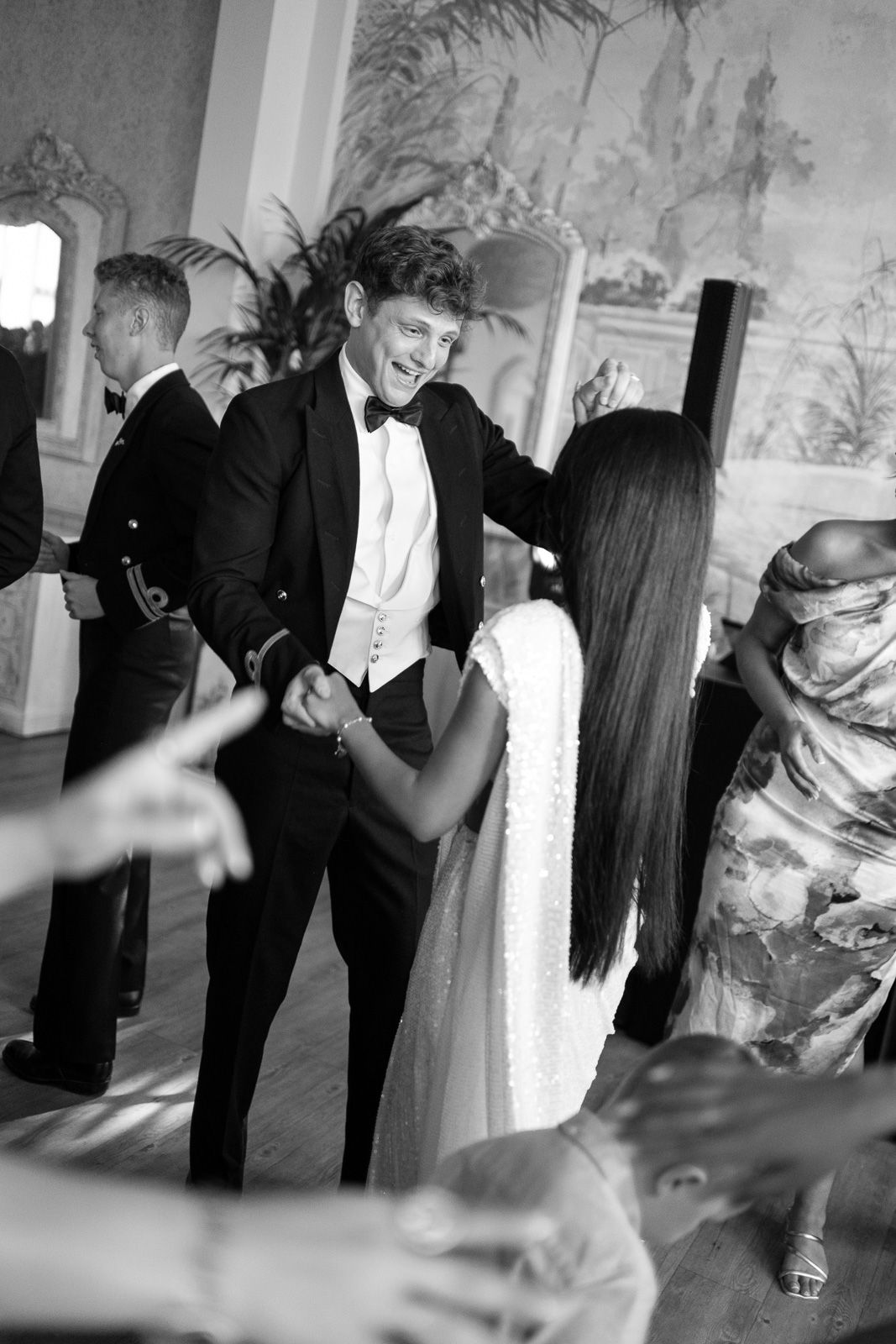 Smiling groom in black tuxedo dances with bride during elegant wedding reception.