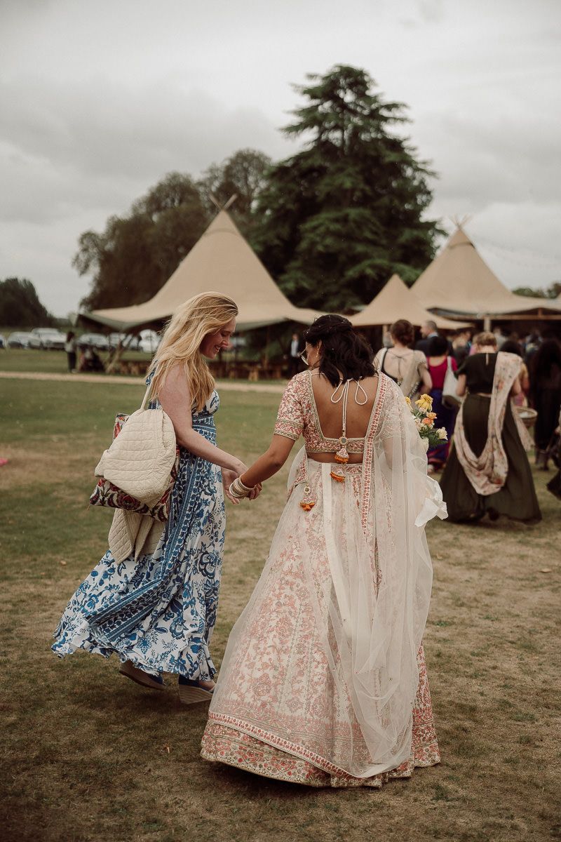 Women in flowing summer dresses dancing together at an outdoor festival with teepee tents in background.