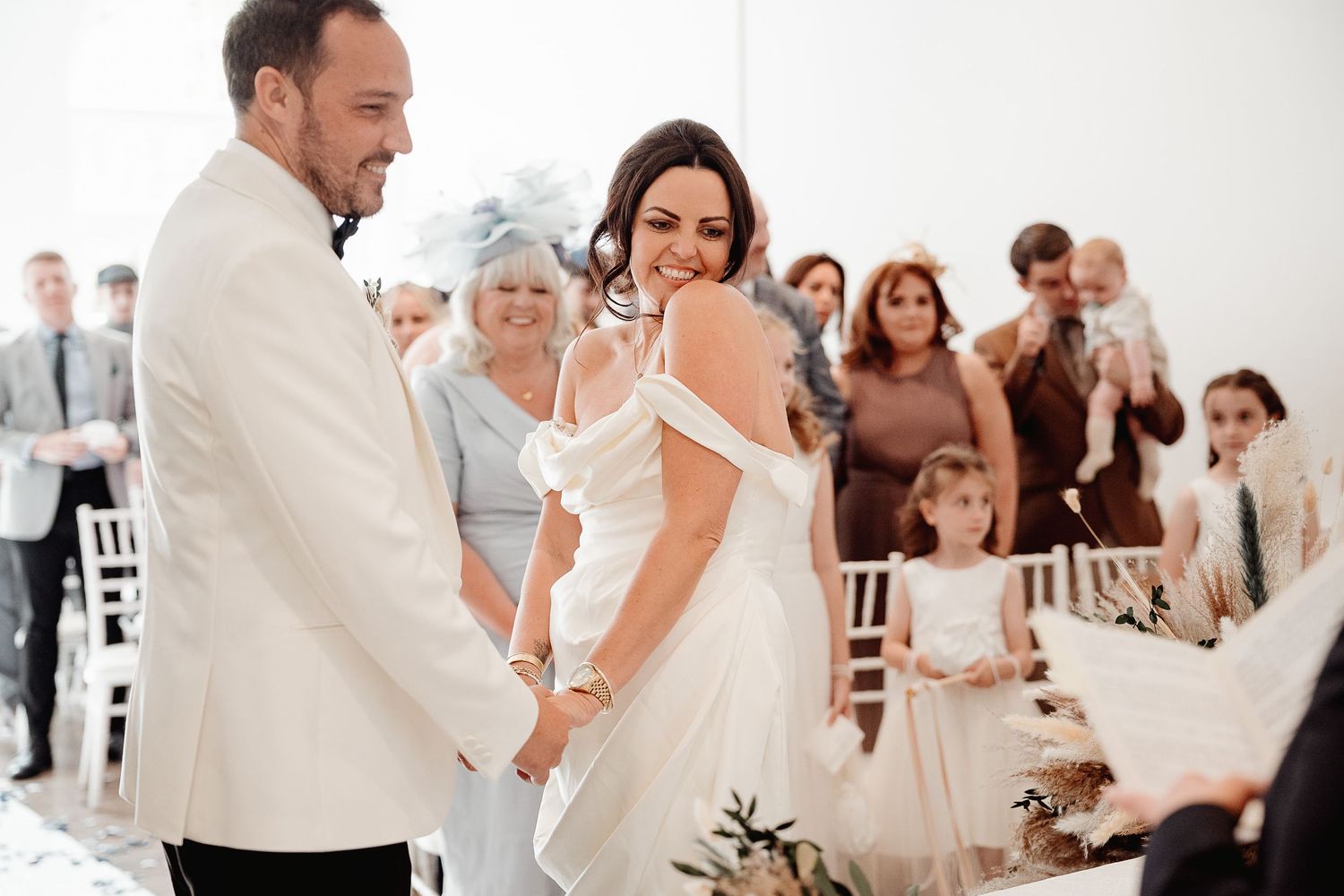 A joyful couple dances at their all-white wedding reception surrounded by their guests.