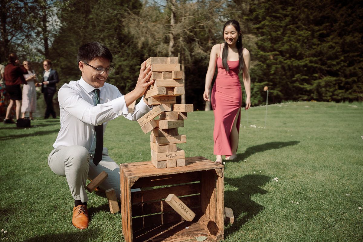 People playing giant Jenga outdoors on a sunny day in a grassy area.