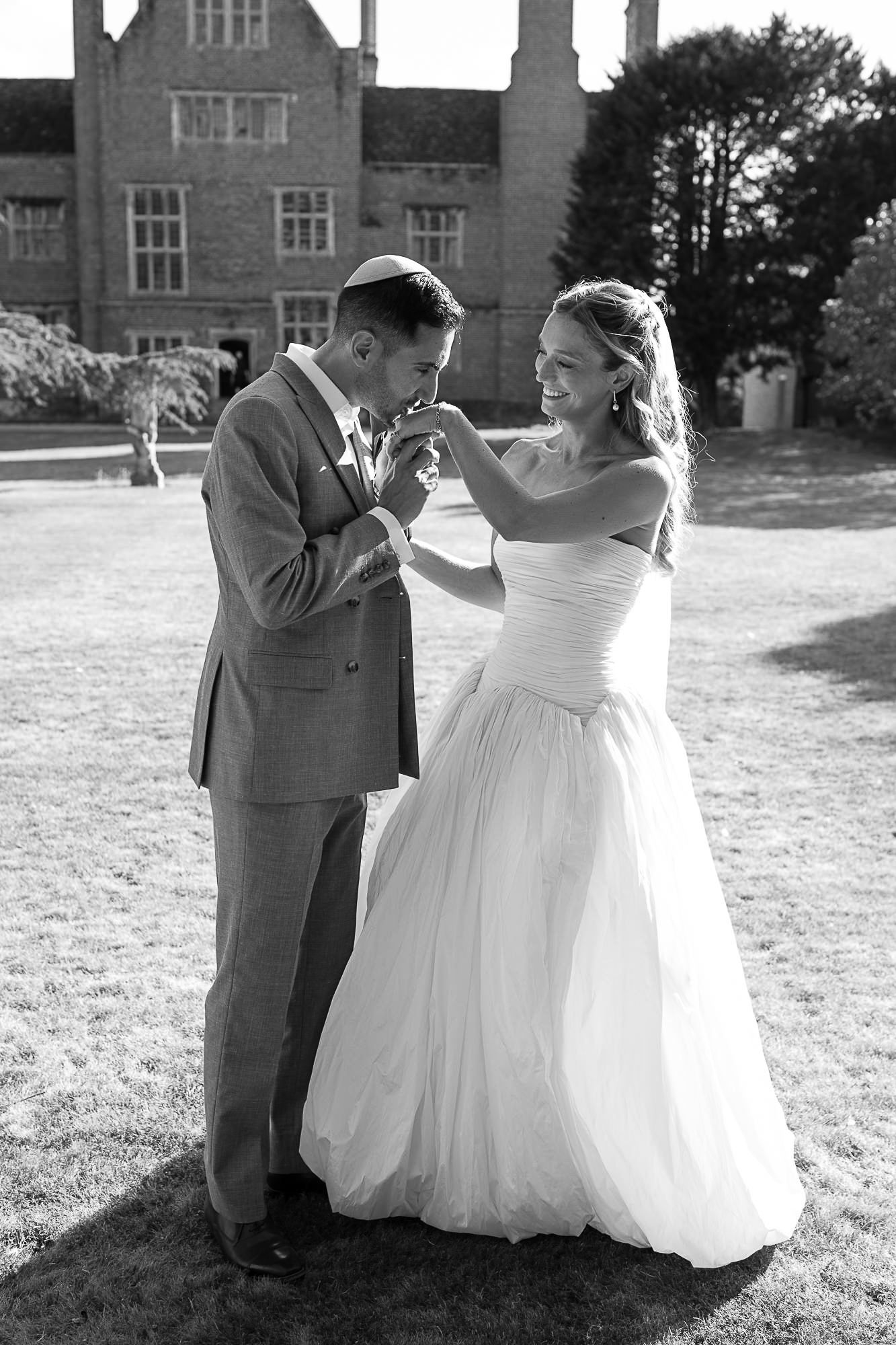 Black and white photo of a bride and groom sharing a tender moment on a lawn outside a historic manor house.