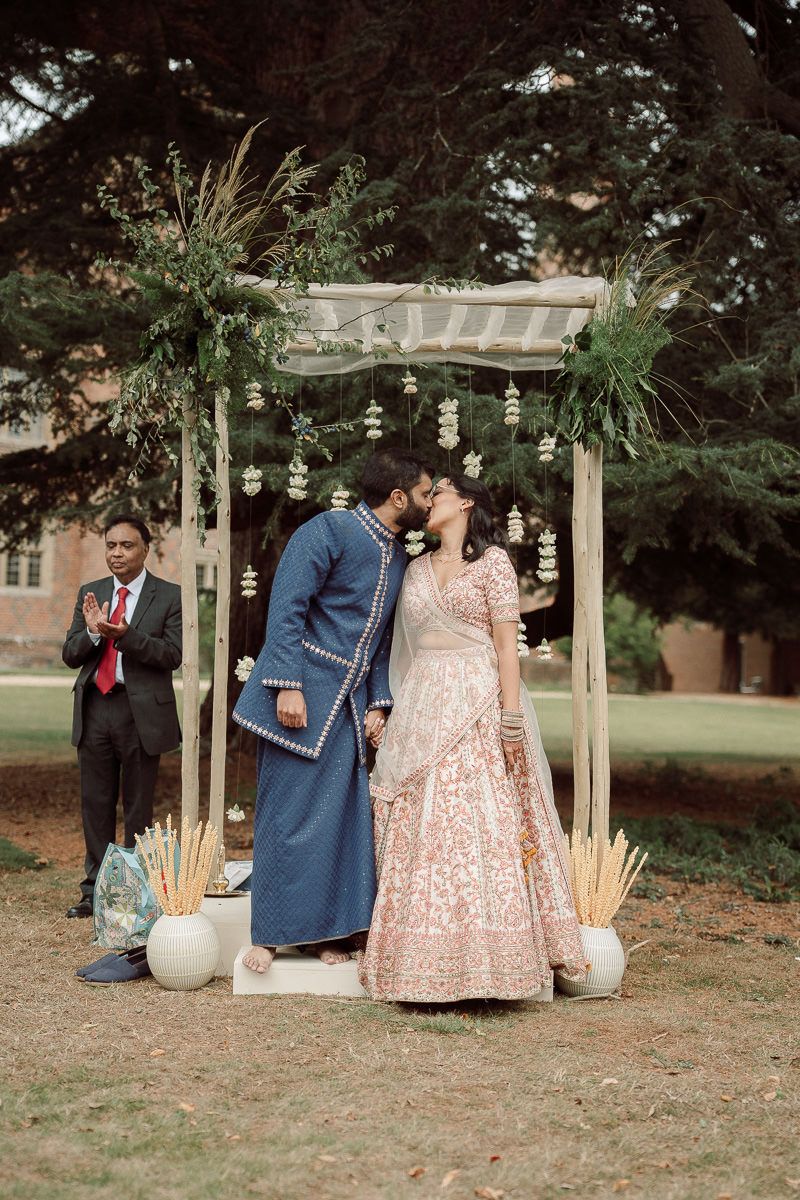 A romantic outdoor wedding ceremony setup with a wooden pergola and hanging lanterns in a garden setting.