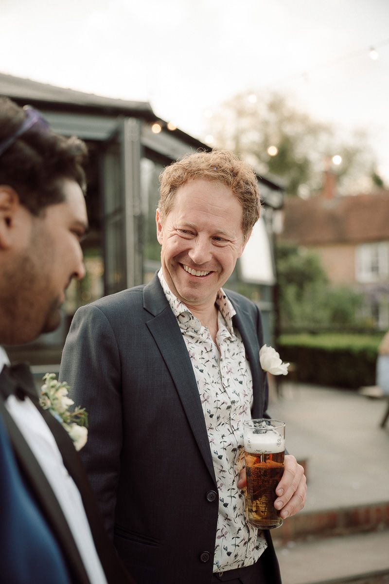 A group of guests share drinks and laughter at an outdoor wedding reception.