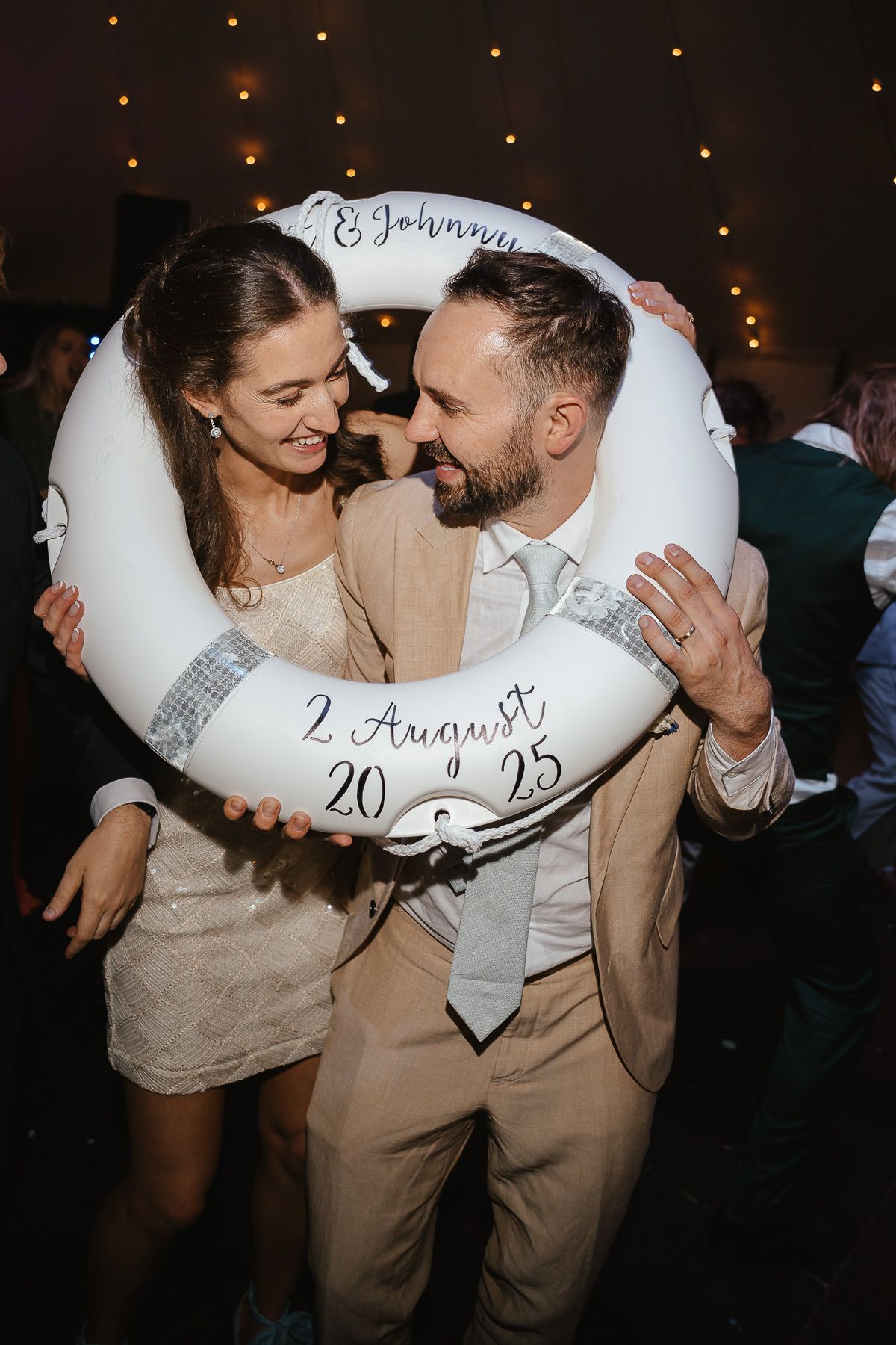 Romantic couple shares intimate moment at wedding reception with string lights glowing in background.