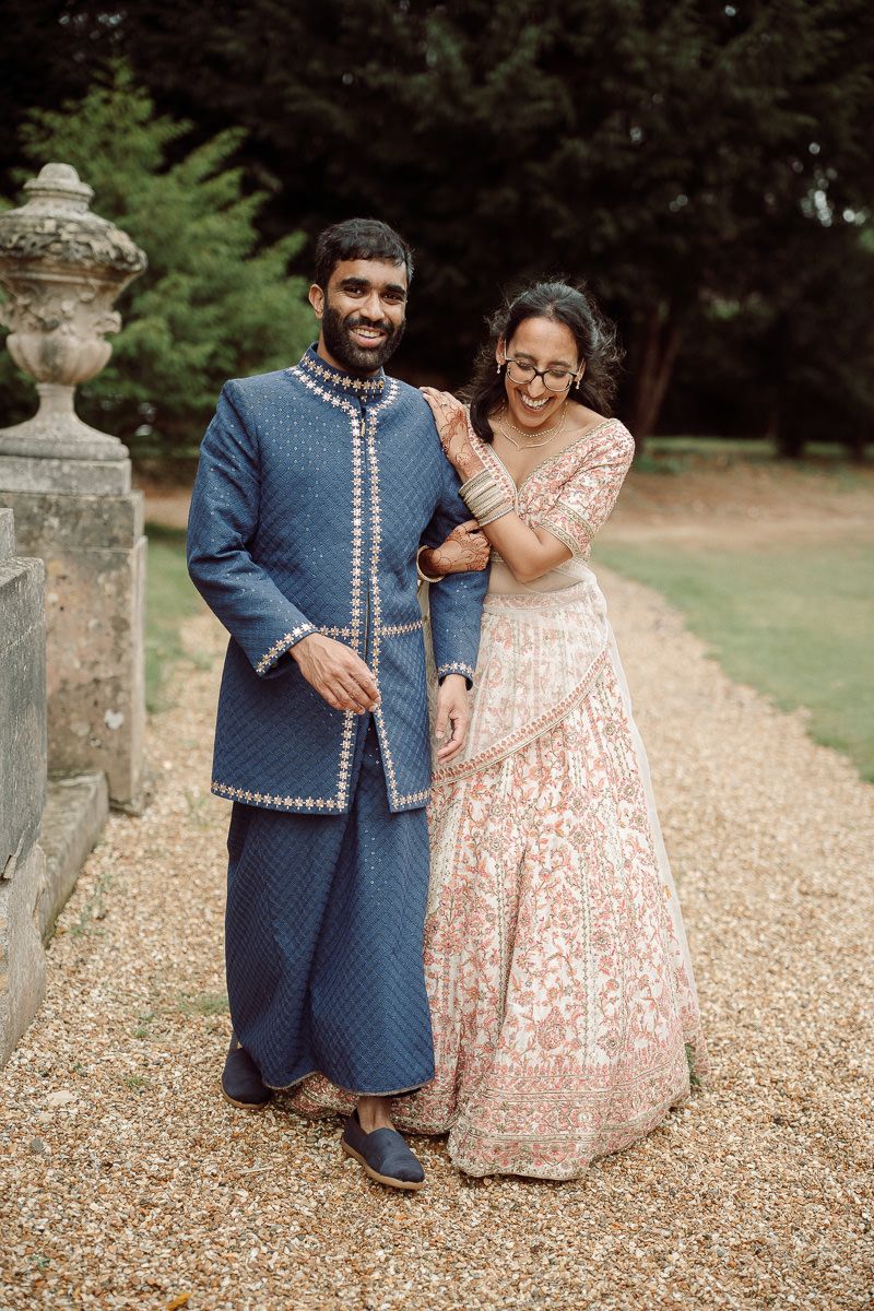 Couple in traditional wedding attire walking along stone-lined garden path.