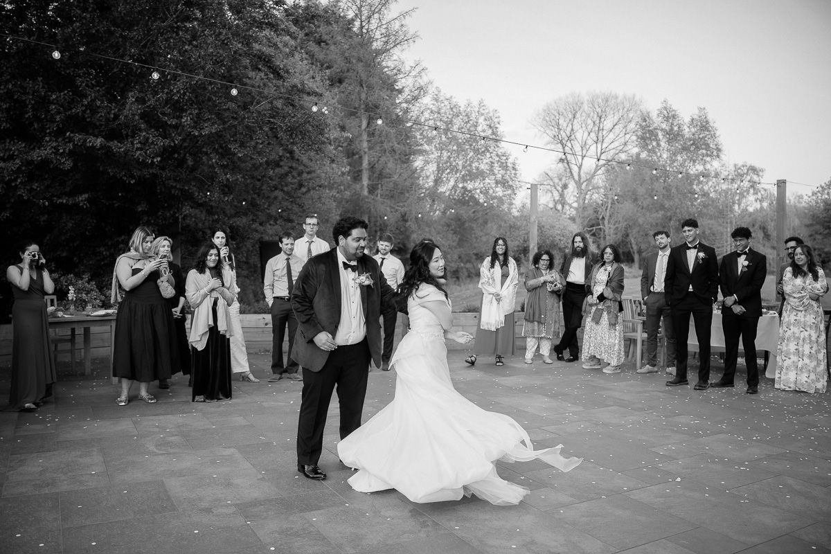 A black and white panoramic sequence of a wedding celebration in an outdoor garden setting with trees in the background.