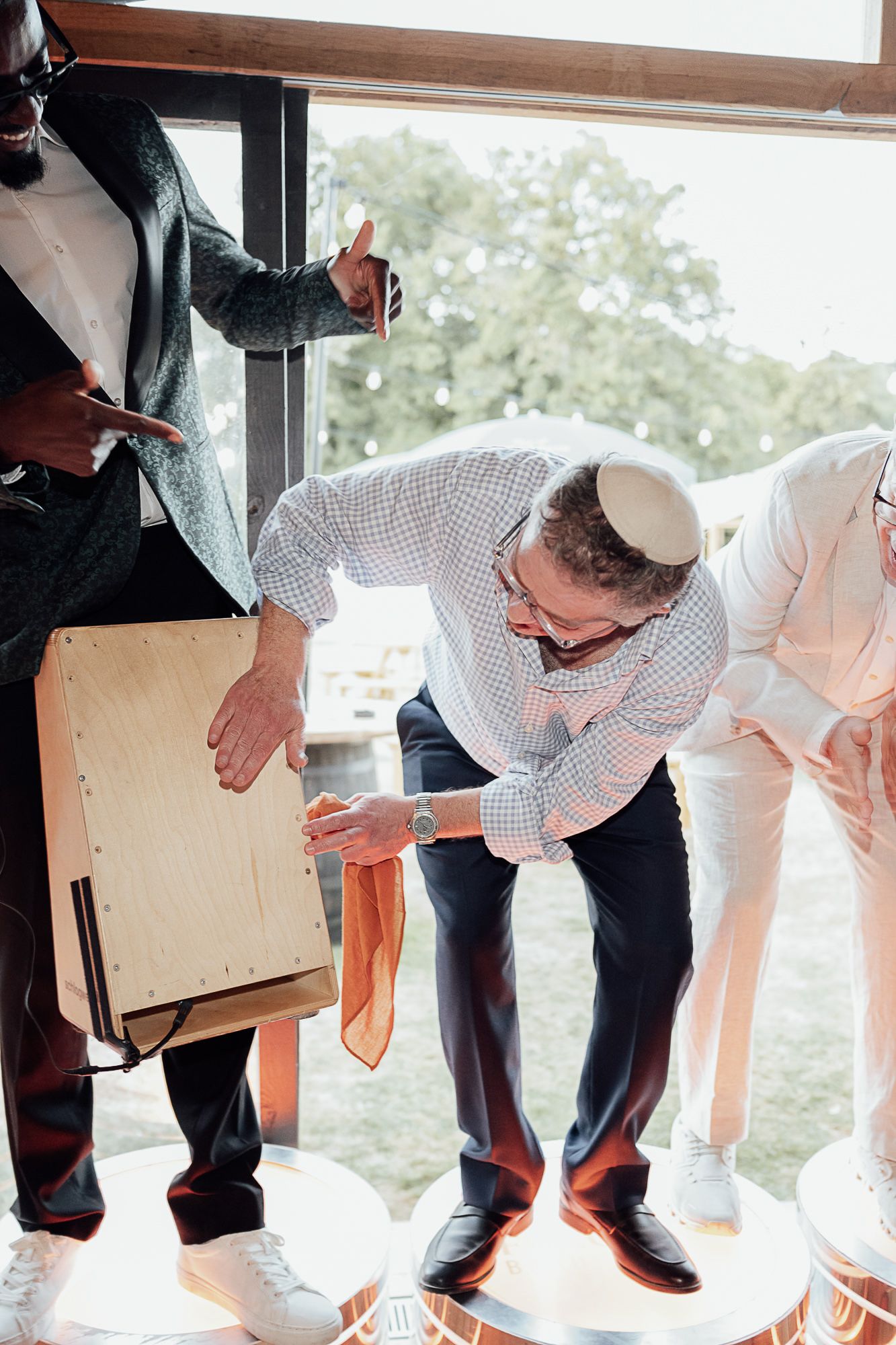Man wearing kippah plays a cajon percussion instrument at a Jewish wedding celebration indoors.