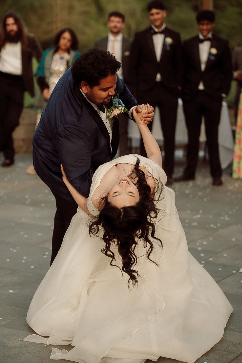 A couple performs a romantic dip dance move at their wedding while guests look on in the background.