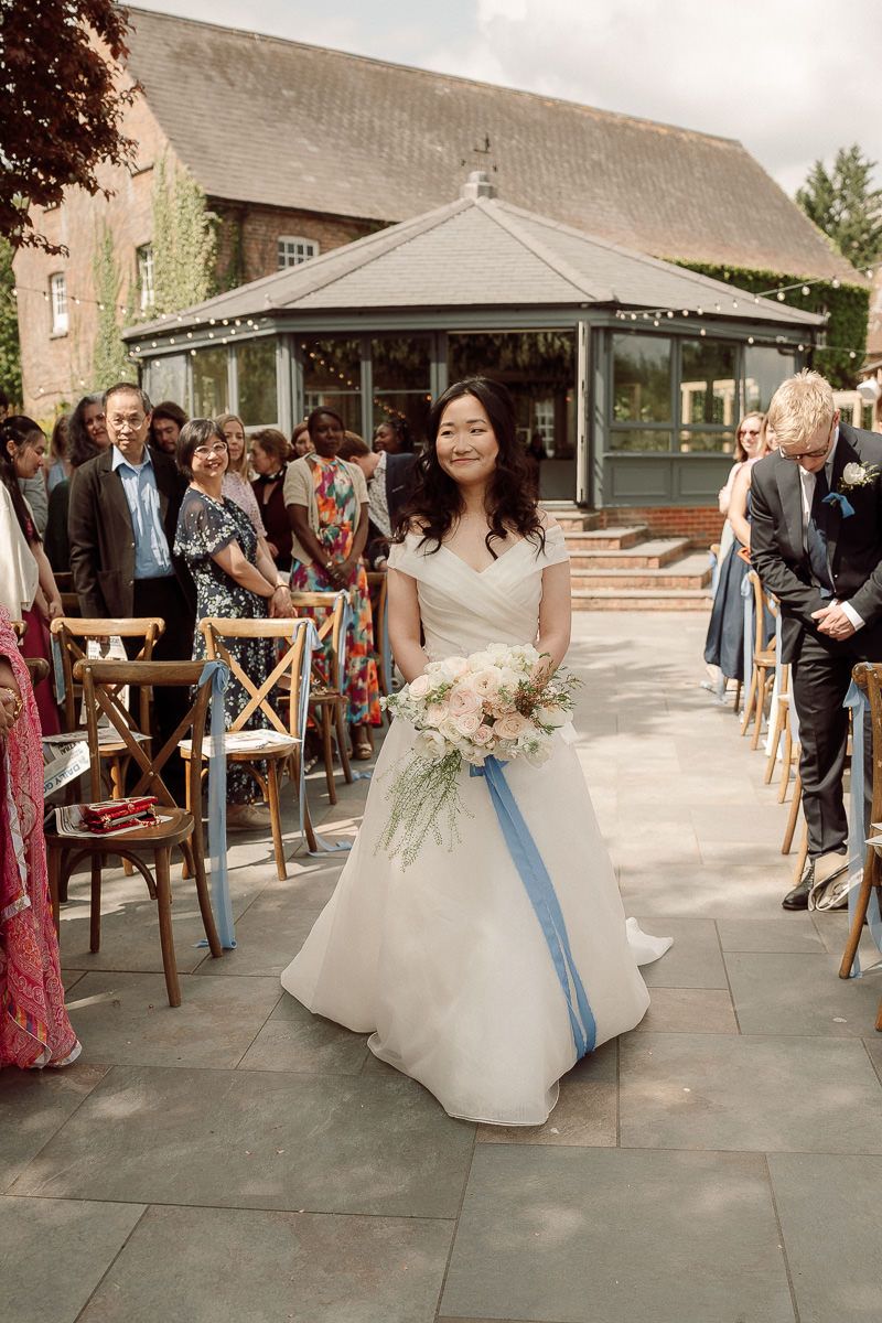 Wedding guests line a walkway as a couple exits their outdoor ceremony with a blue ribbon trailing behind.