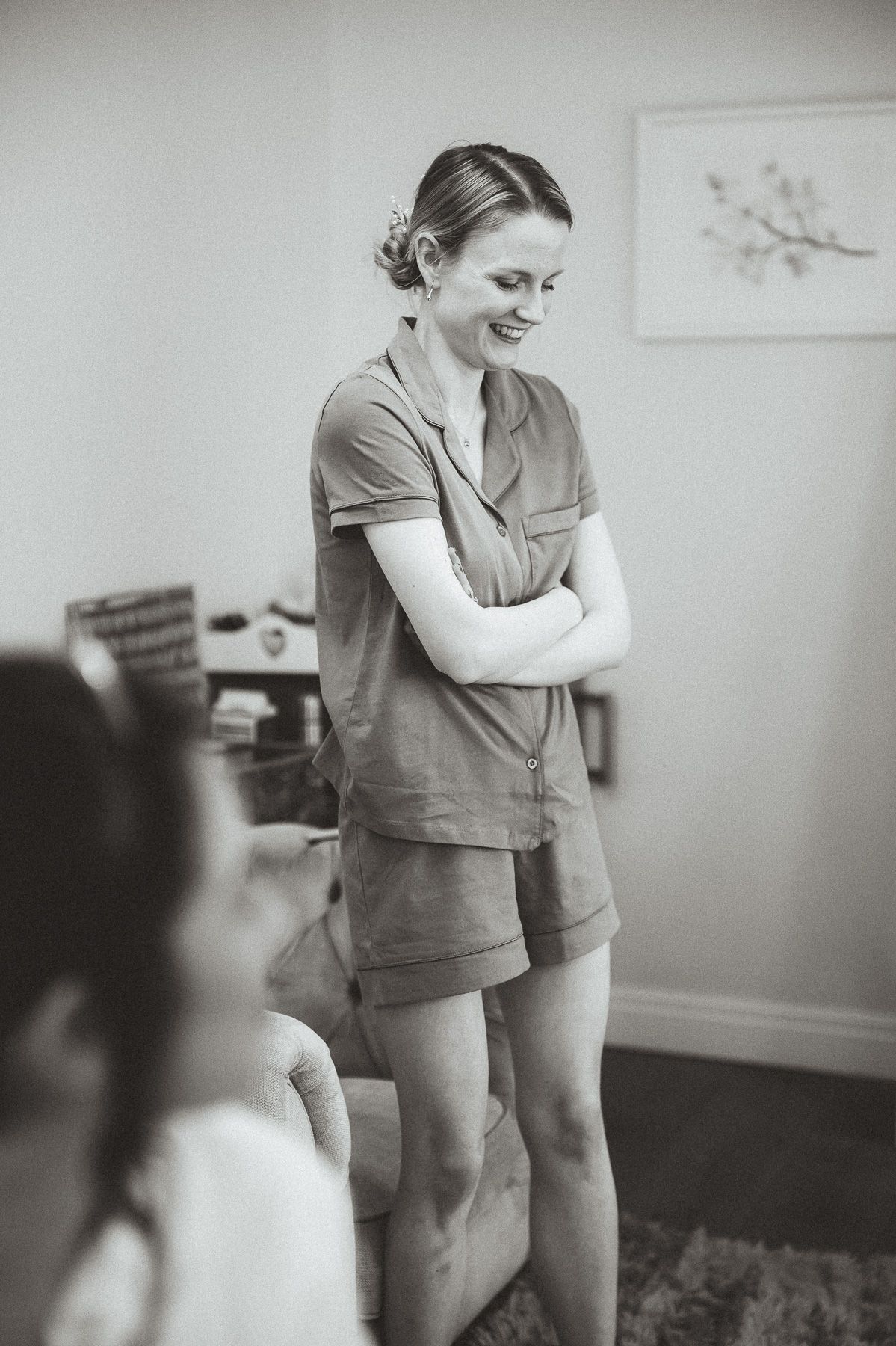 A black and white photo of someone wearing a casual short sleeve outfit standing against a wall with artwork.