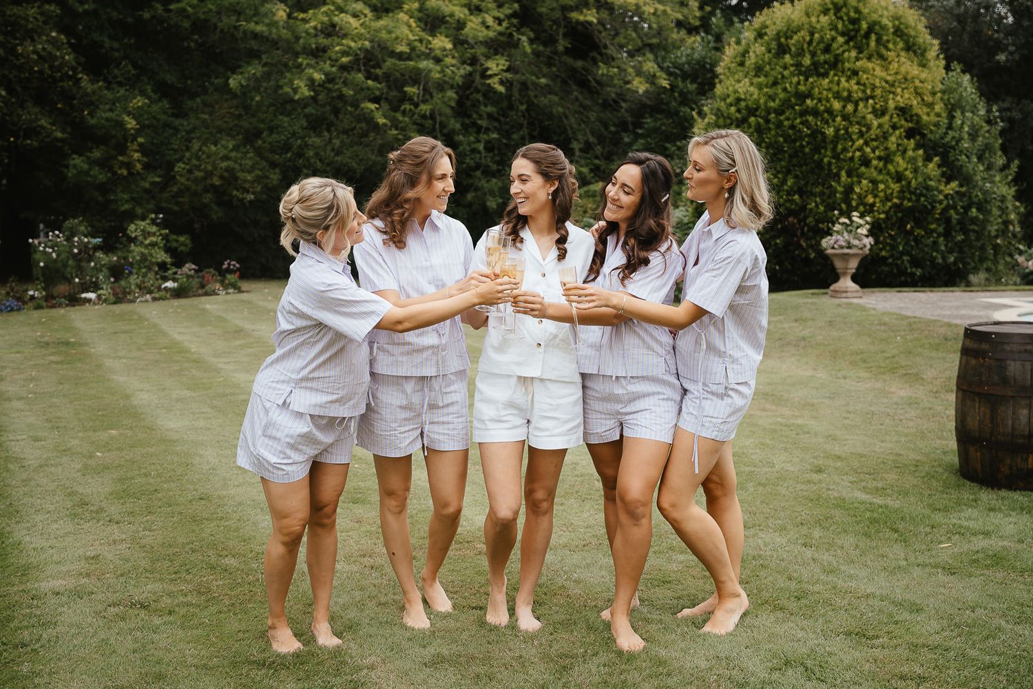 A group in matching white outfits walks arm-in-arm across a sunny lawn during an outdoor celebration.