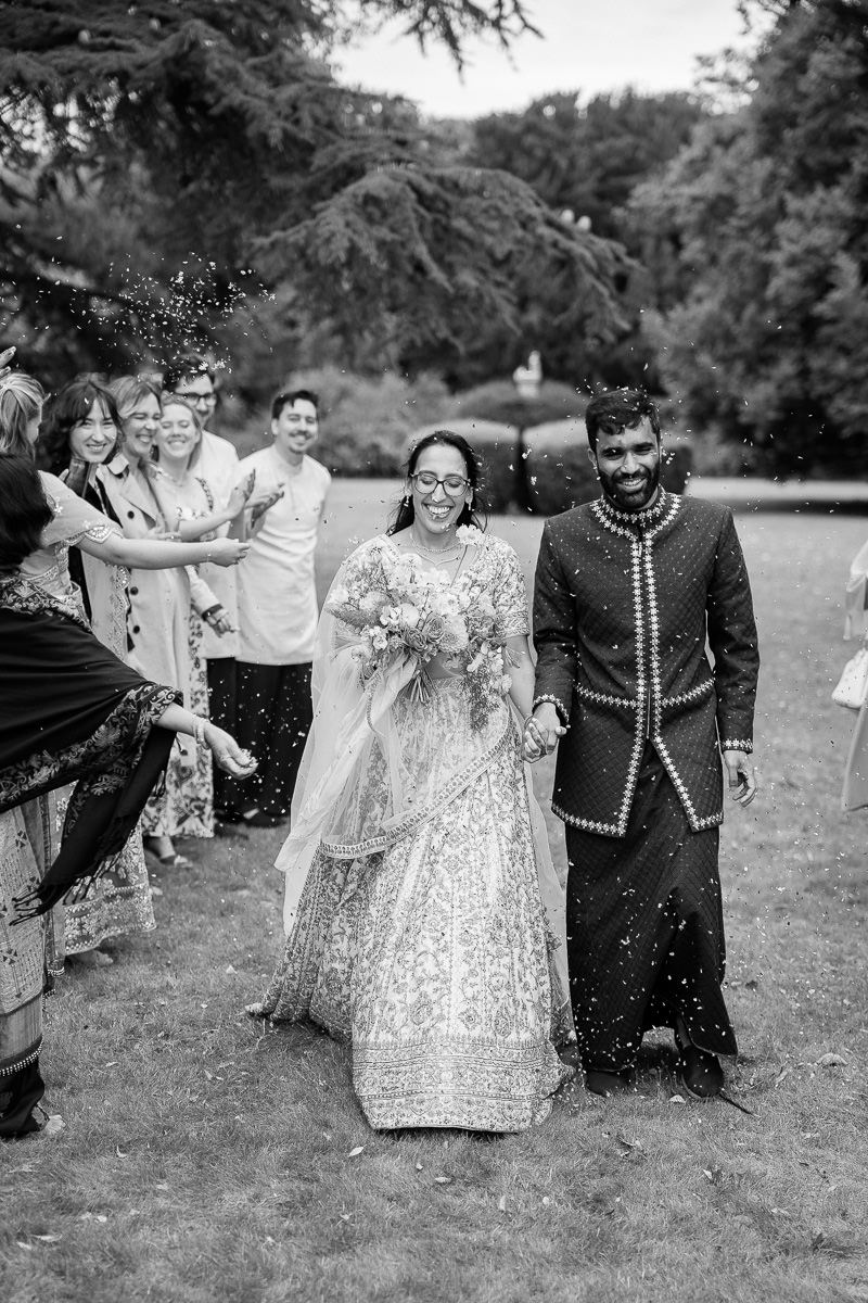 A joyful wedding party in formal attire poses and laughs together in a black and white photo  at mapledurham house wedding venue.