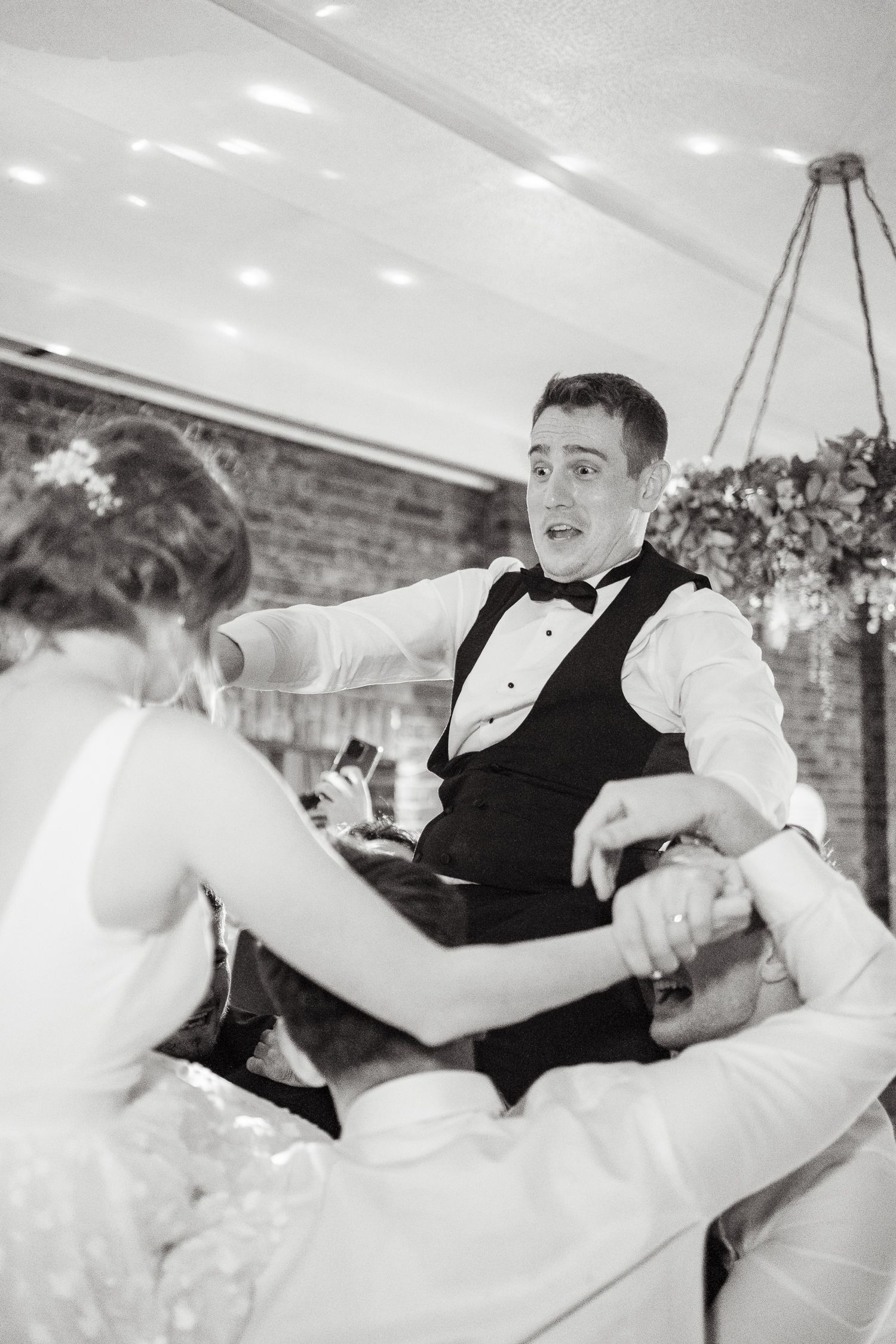 A joyful black and white candid moment of dancing at a formal wedding reception.