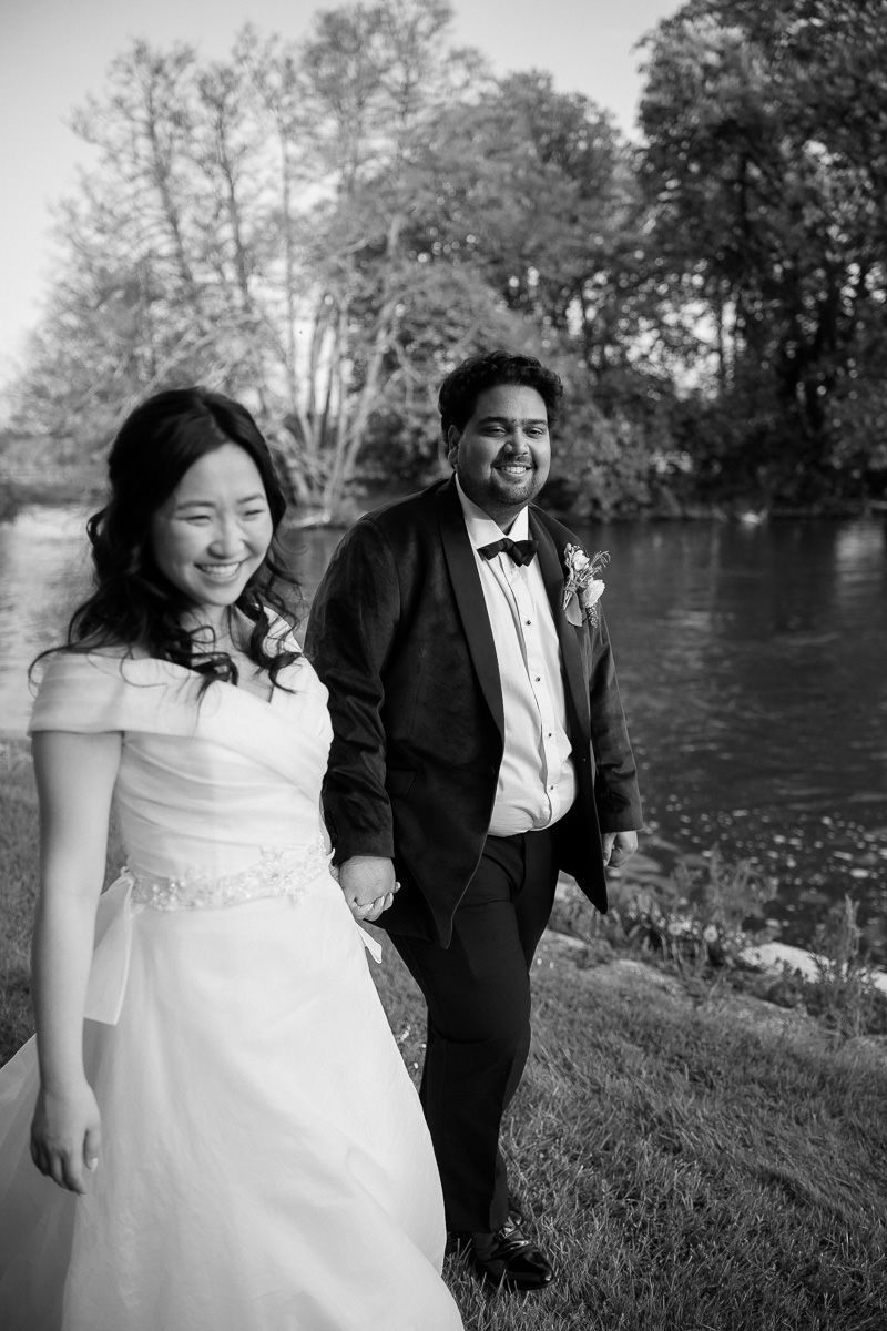 A joyful wedding couple shares candid moments in black and white photography by a lake.