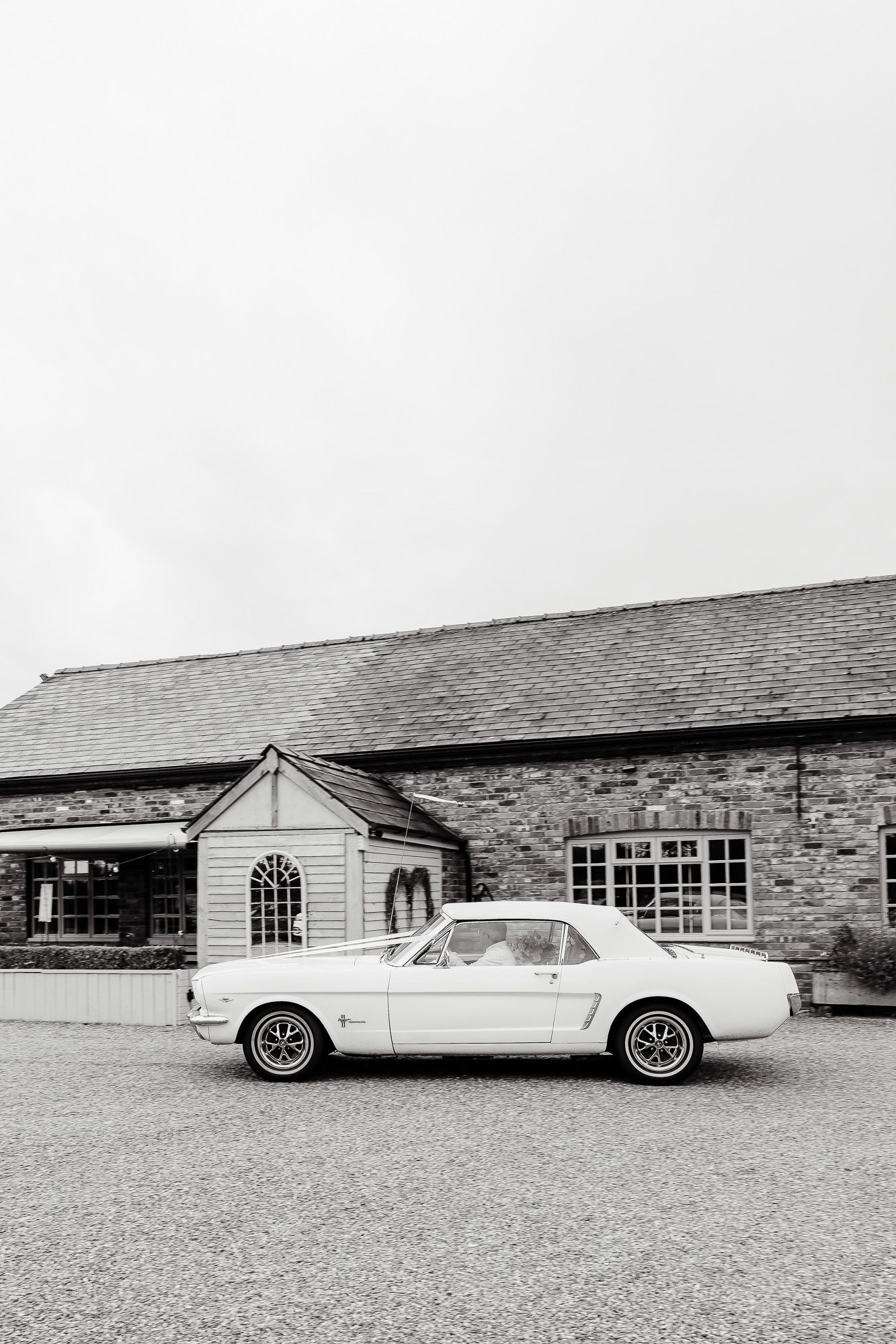 Classic white Ford Mustang parked in front of a rustic stone building with white trim entrance.
