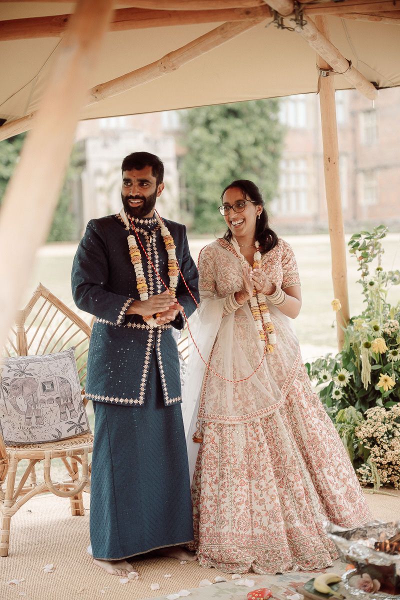 Couple in traditional Indian wedding attire sharing a tender moment under a covered outdoor venue.