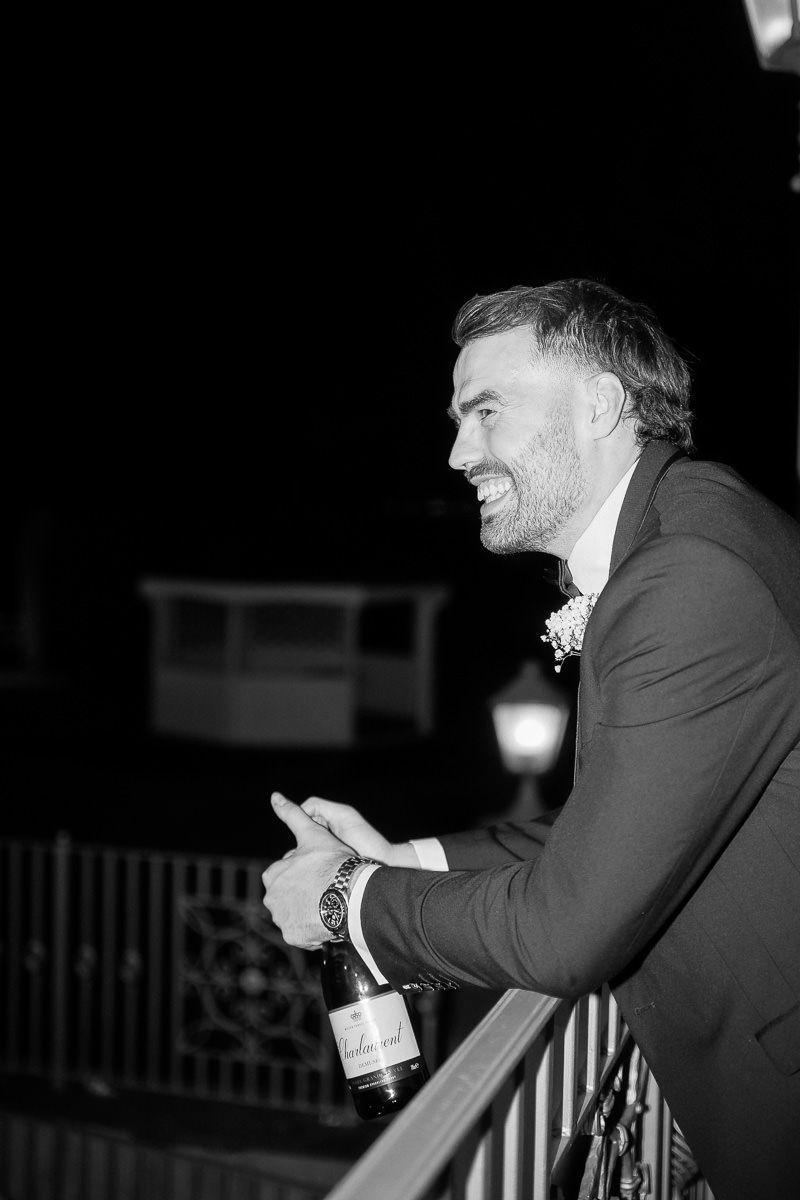 A person in a suit smiles and leans on a railing in a black and white photograph.