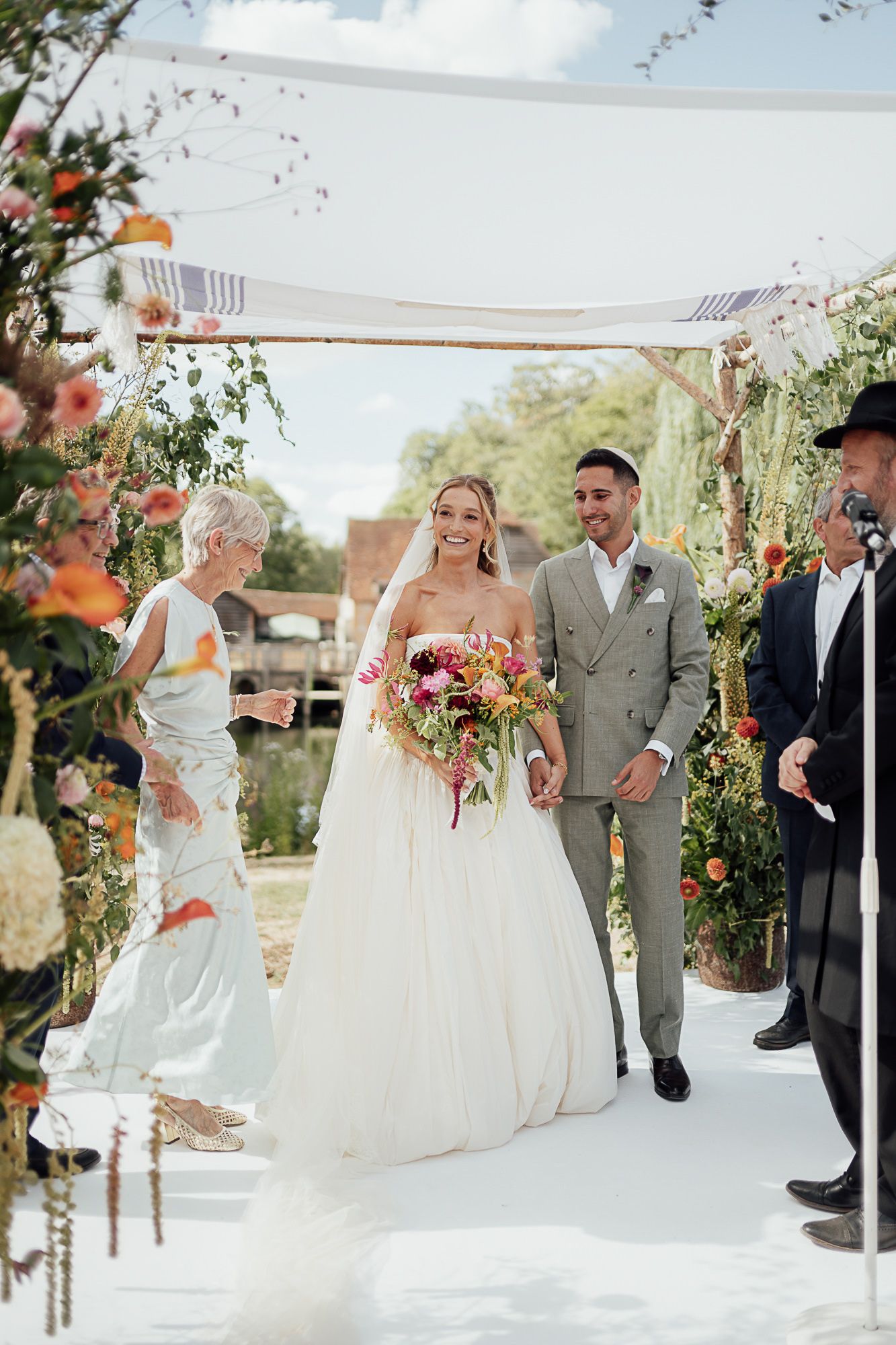Bride and groom walk down the aisle under a floral arch at an outdoor wedding ceremony.