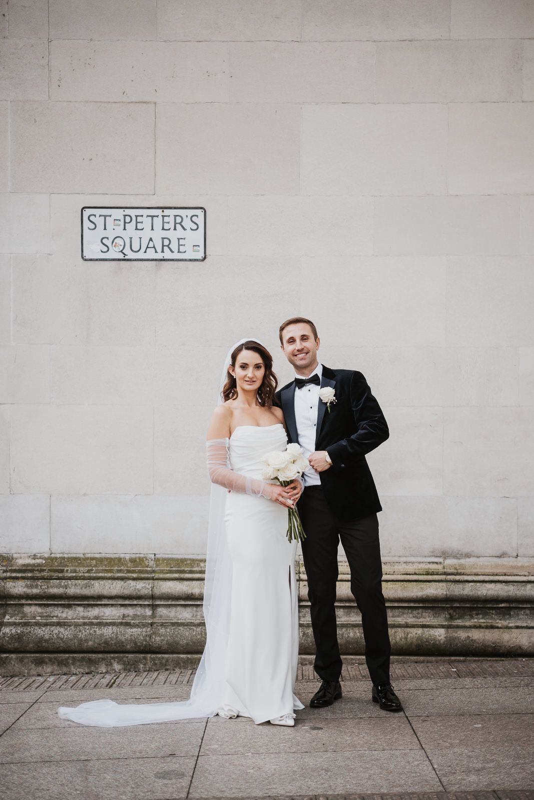 A wedding couple standing next to a St. Peters Square sign on a stone wall on their special day.