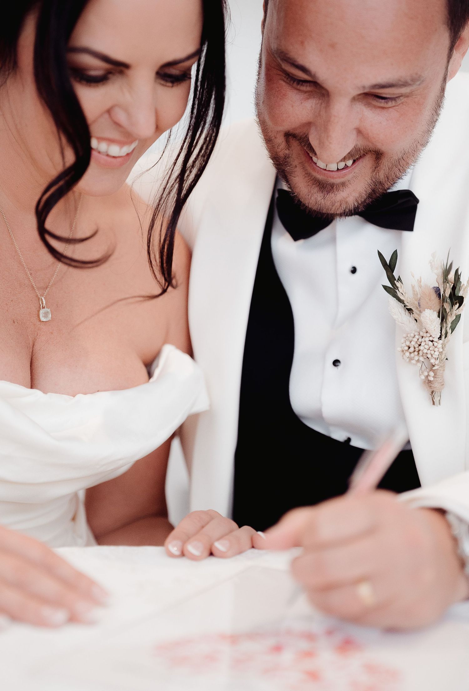 A bride and groom lean in close together while signing their marriage documents at their wedding ceremony.
