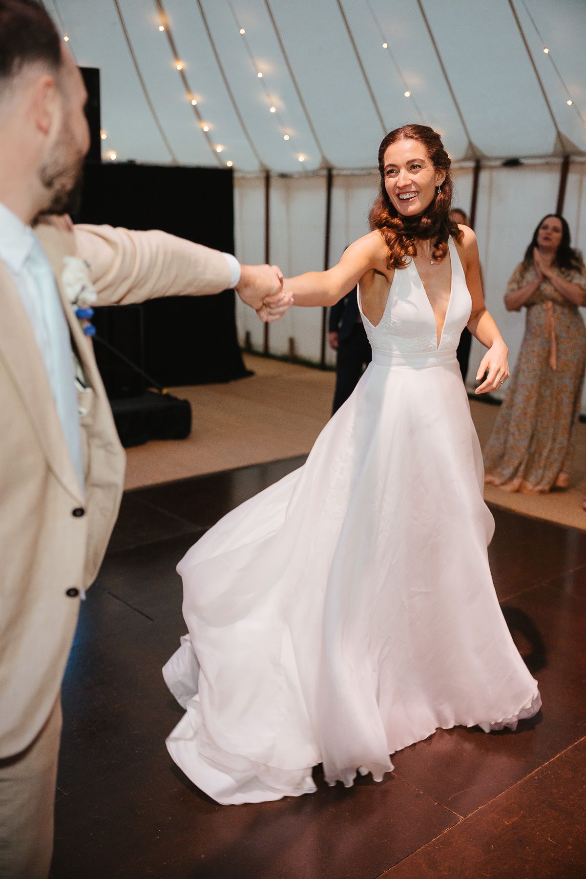 A bride and groom share a romantic dance together on a polished wood floor under a white tent during their wedding reception.