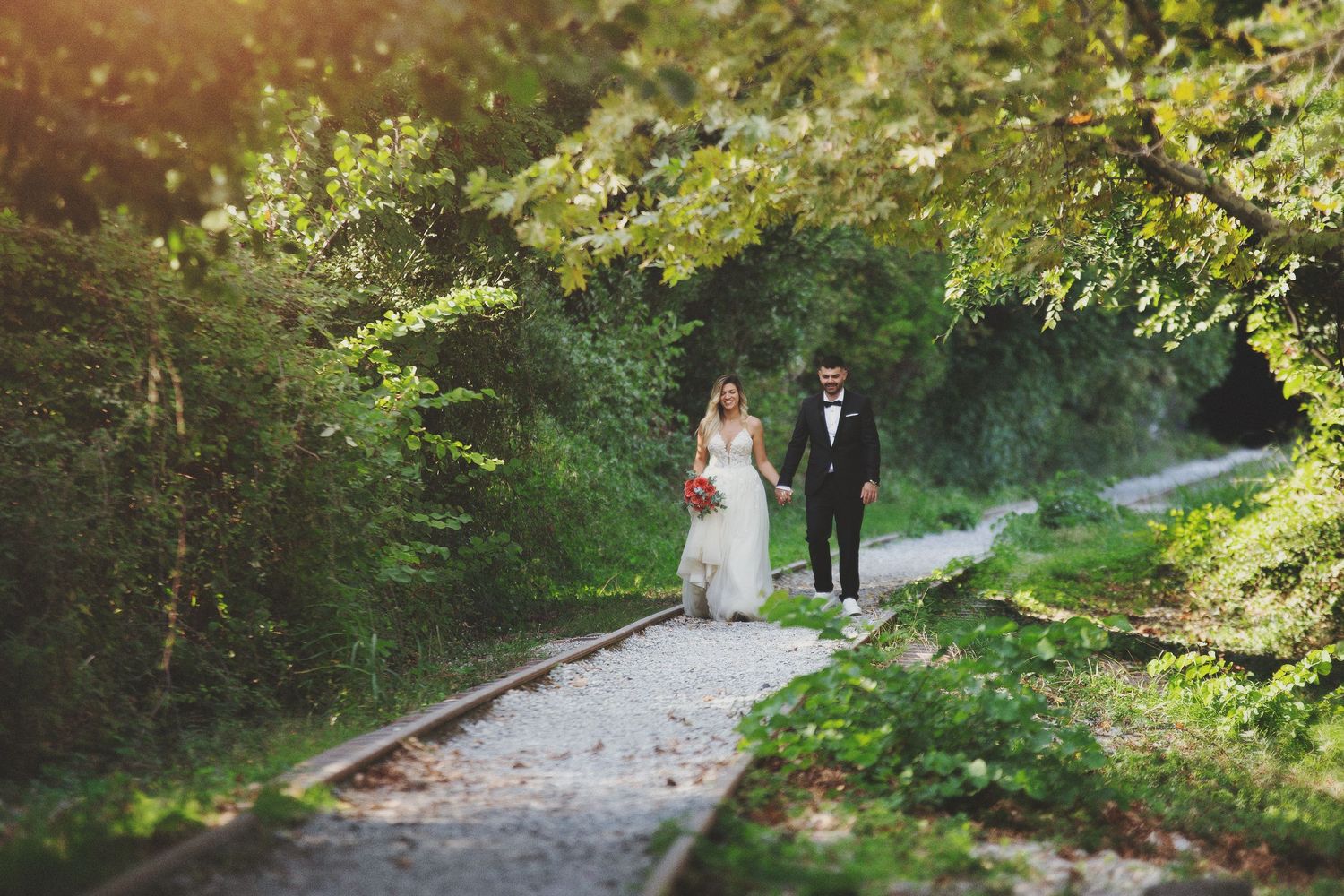 Moody fine art wedding portrait of a romantic couple walking through a lush green nature path with a film look.