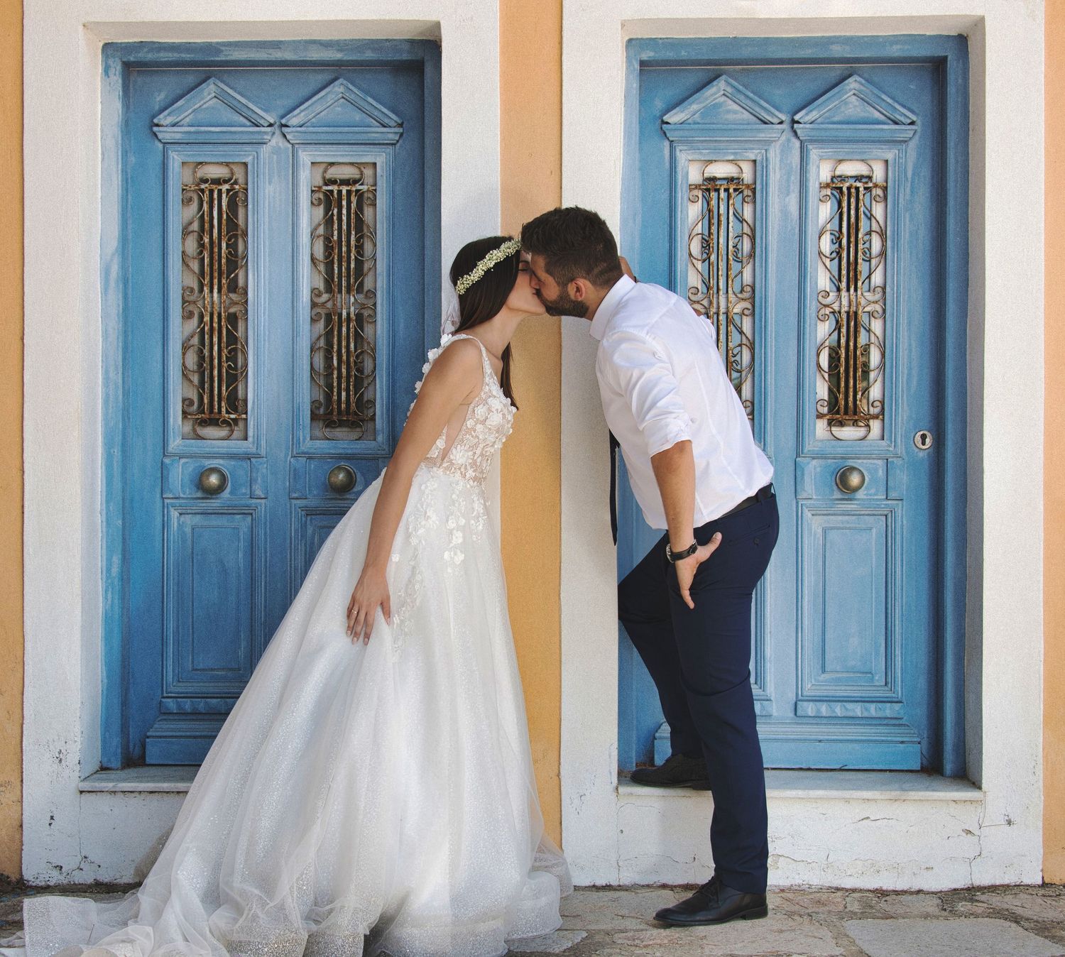 Greek island destination wedding photography featuring a bride and groom kissing in front of traditional blue doors.