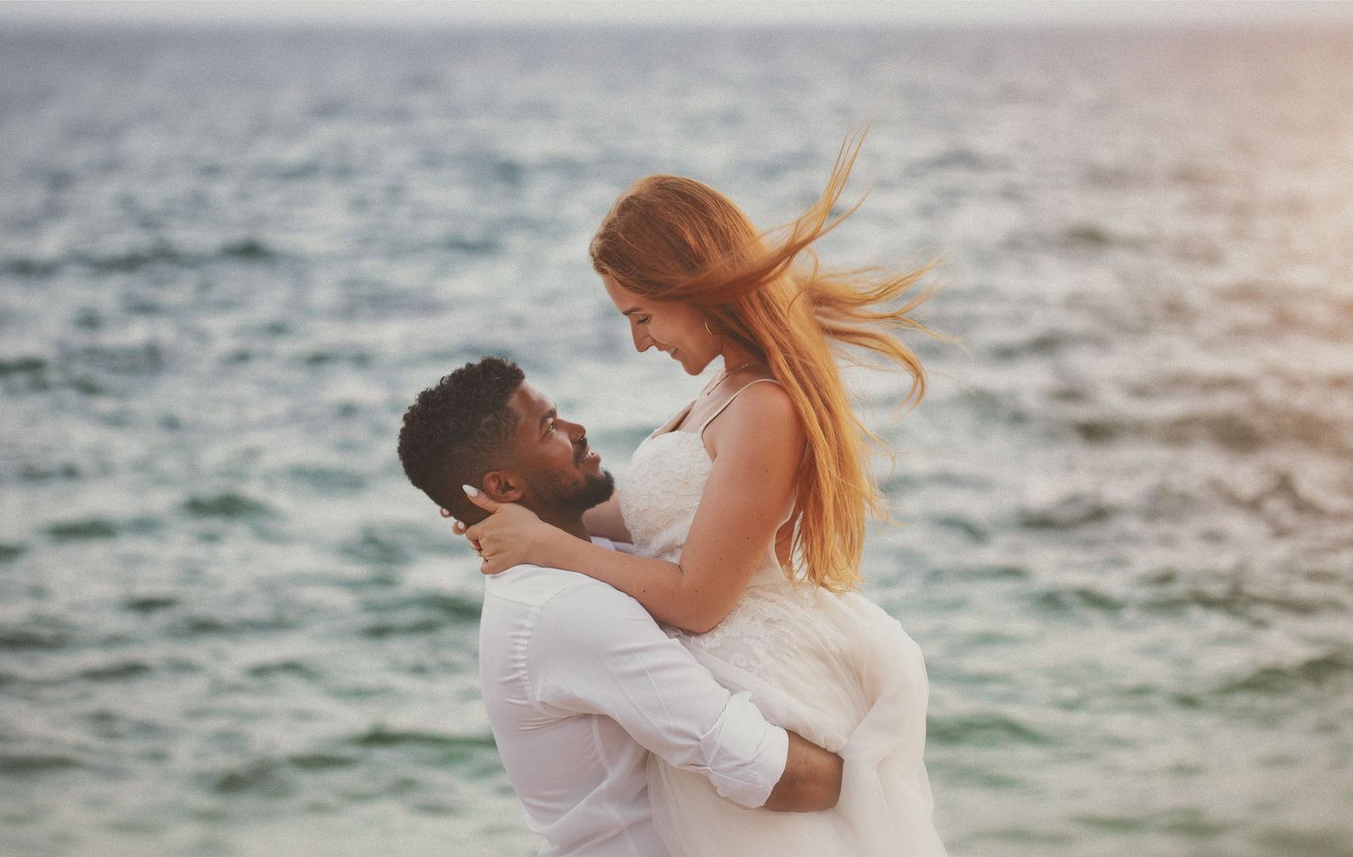 Documentary beach wedding photography of a groom lifting his bride in his arms near the sea.