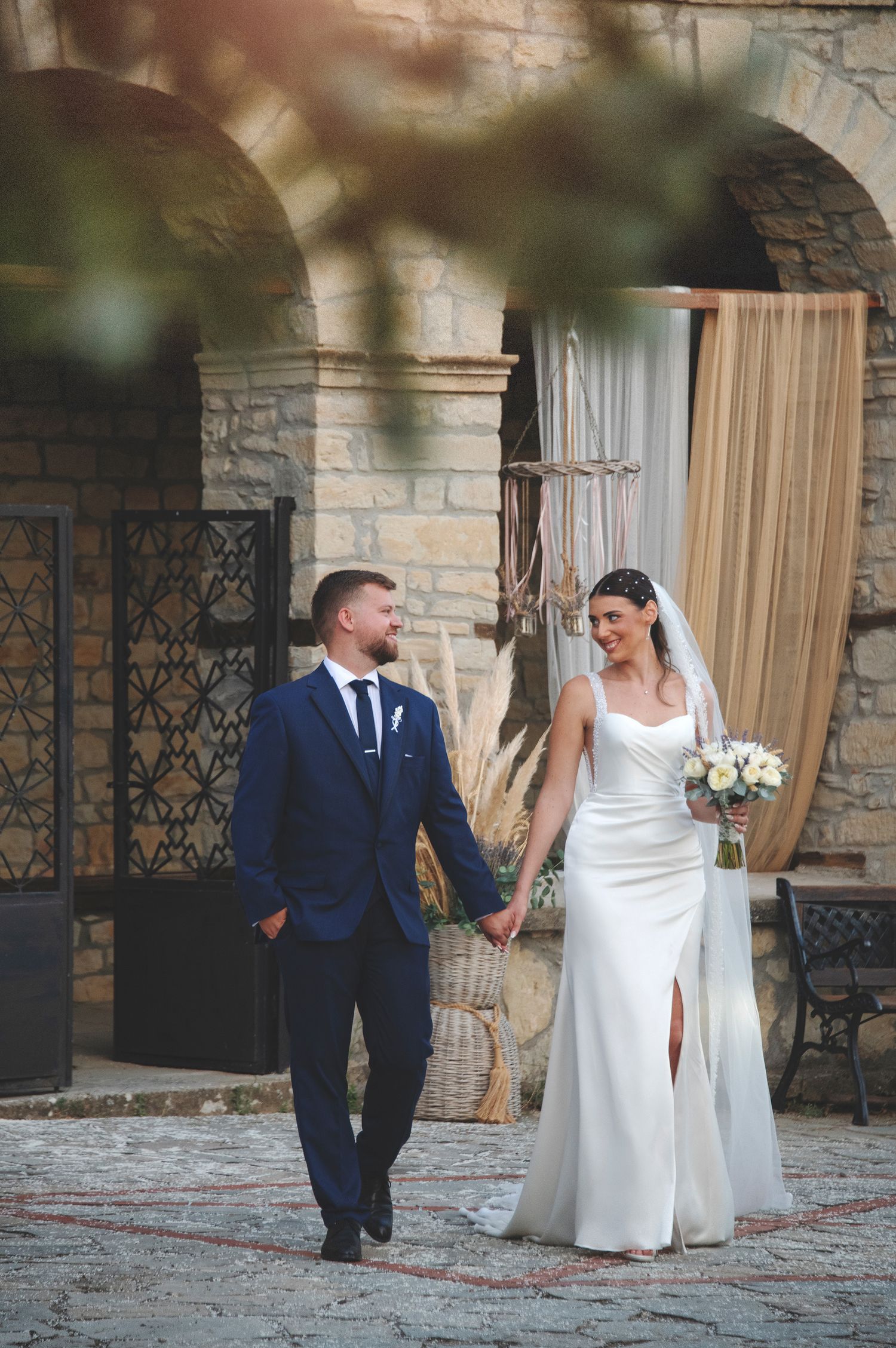 Documentary wedding photography at a stone venue featuring a bride and groom walking hand in hand.